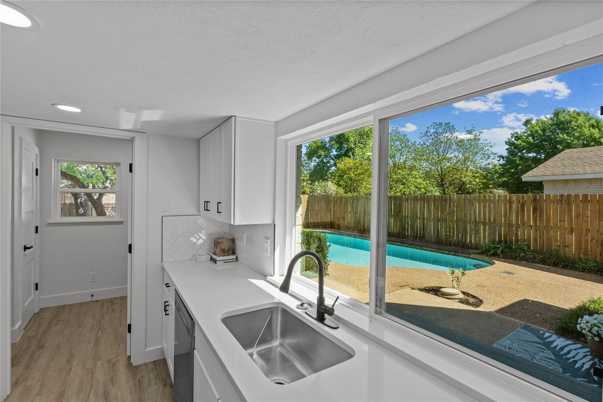 Utility room sink and counter overlooking a fenced backyard pool.