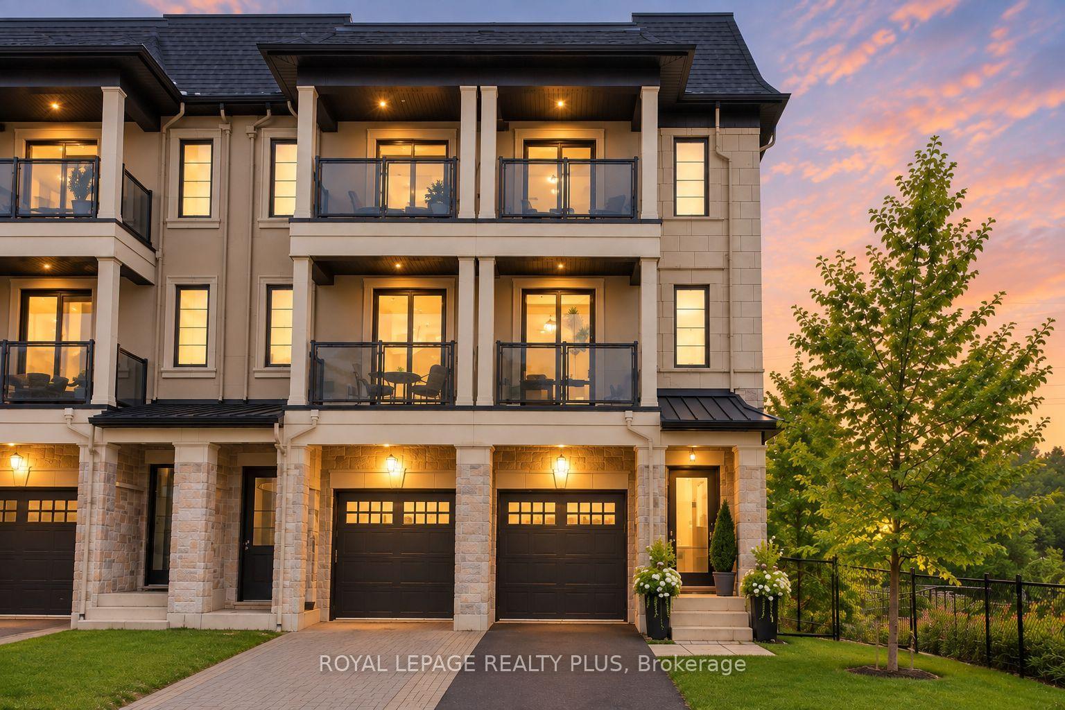 Upscale townhouses with glass balconies and stone façades glowing at dusk beside a leafy tree.
