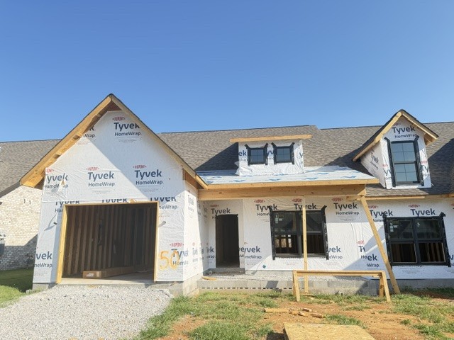 House under construction with Tyvek wrap, front gables, and a gravel driveway.