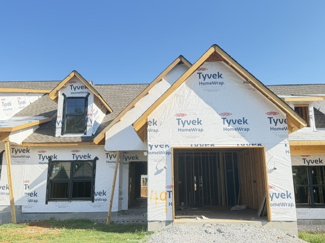 House under construction with Tyvek-wrapped facade, dark windows, and an open garage.