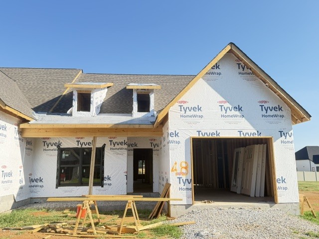 House under construction with Tyvek-wrapped exterior, open garage, and two front dormers.
