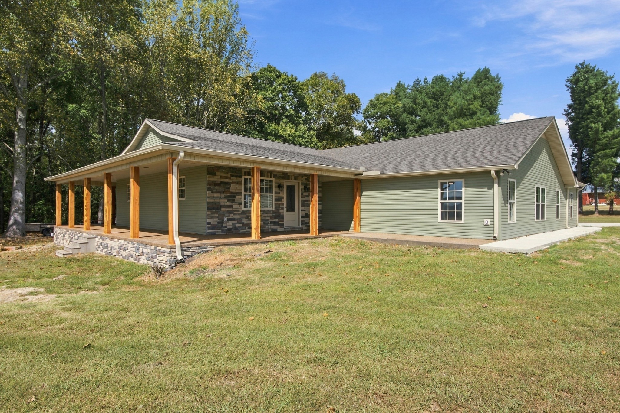 Single-story sage-green house with a stone-accented entrance and a long covered porch.