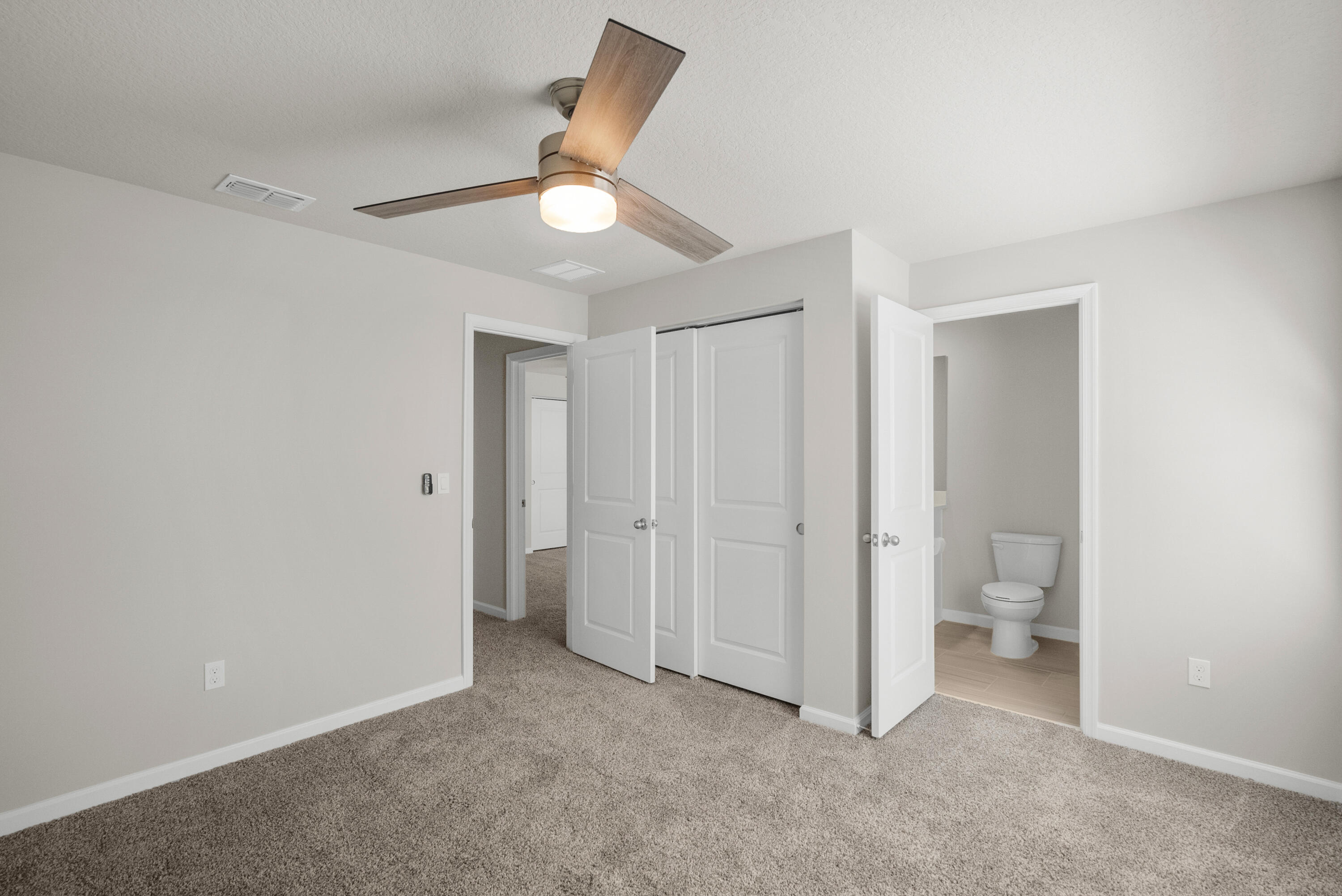 Unfurnished carpeted bedroom with a ceiling fan, open closet, and adjoining bathroom.