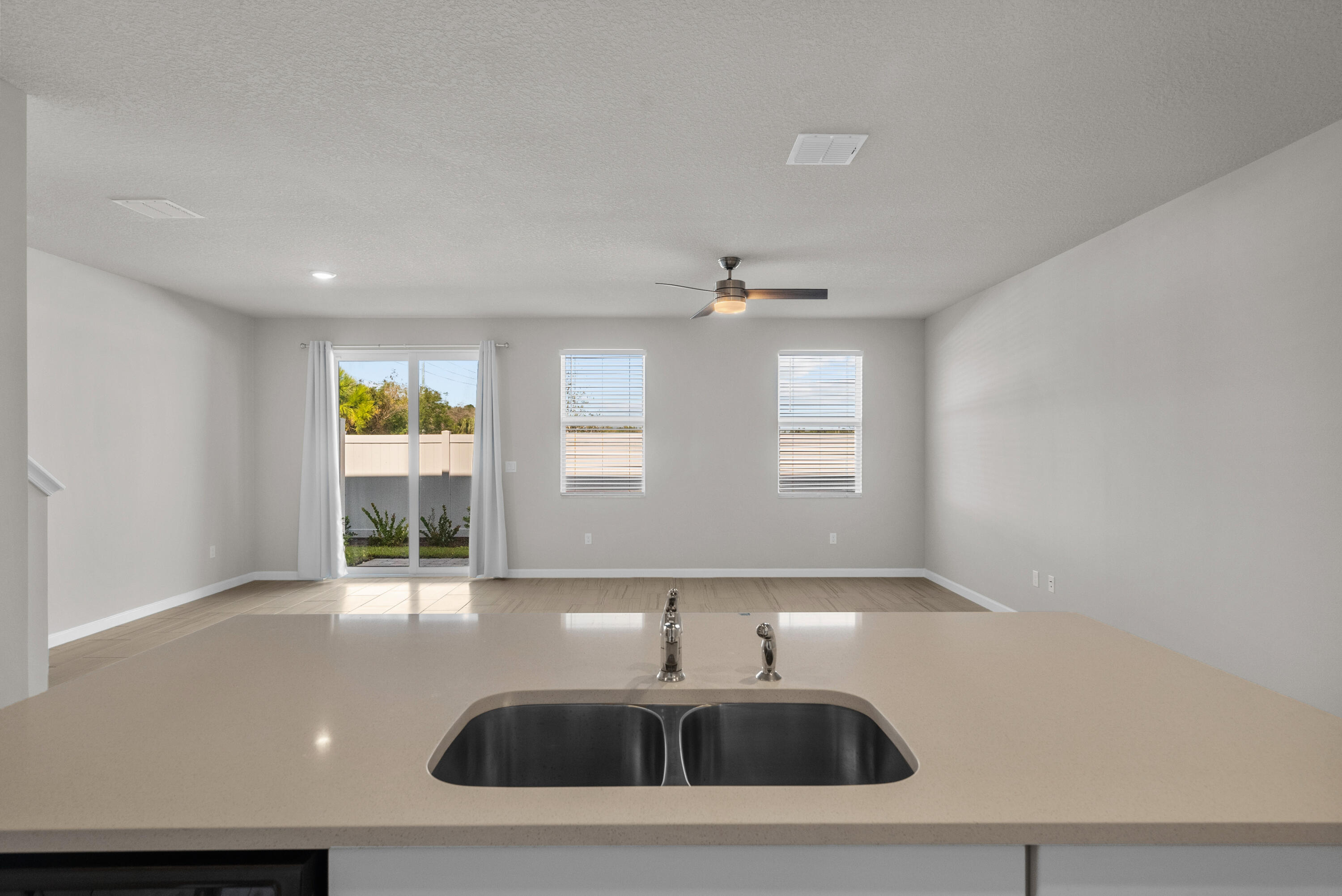 Kitchen with a double-basin sink overlooking an empty living area and sliding glass doors.