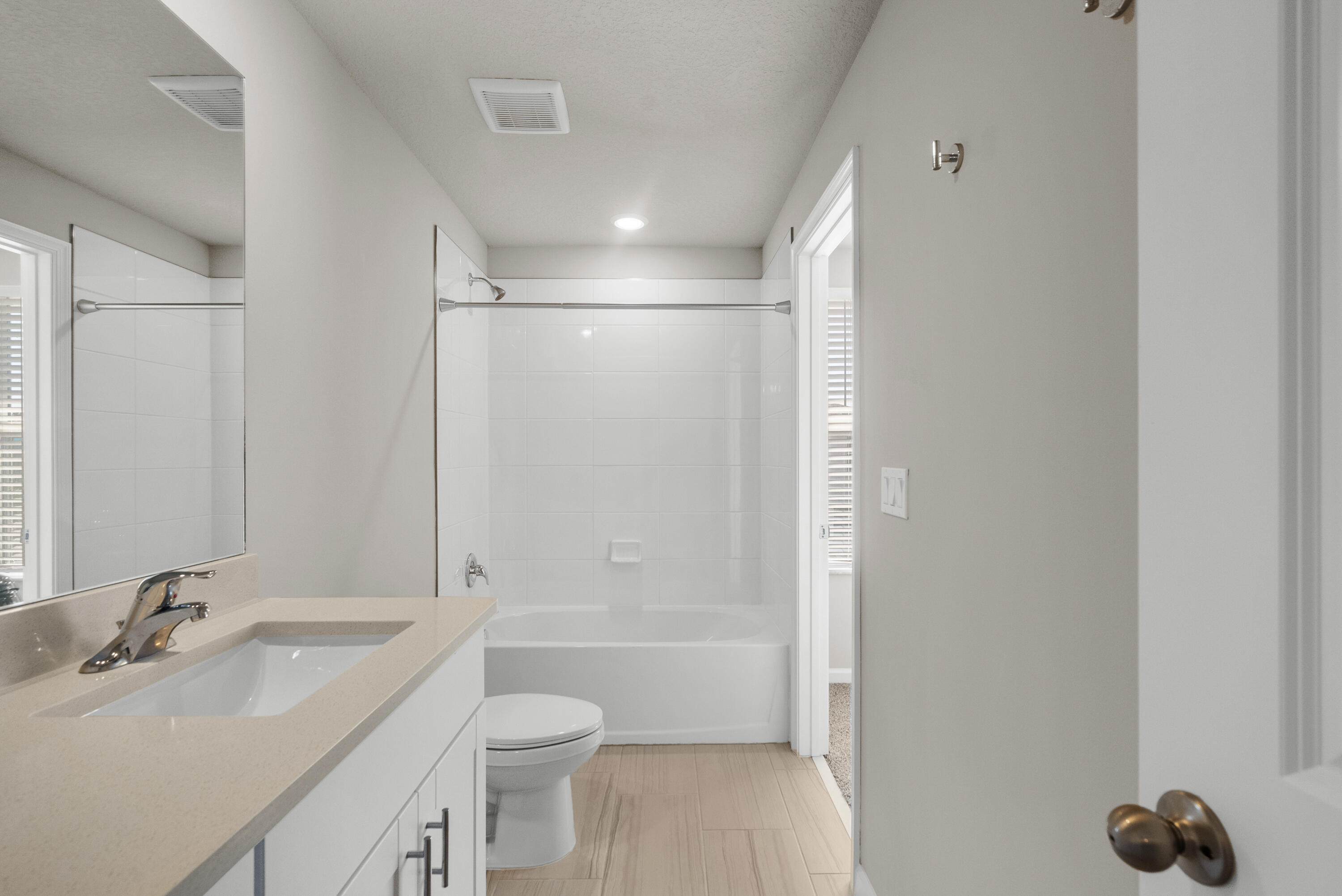 Bathroom with a white tub and tiled surround, beige vanity countertop, large mirror, and light wood-look floor.