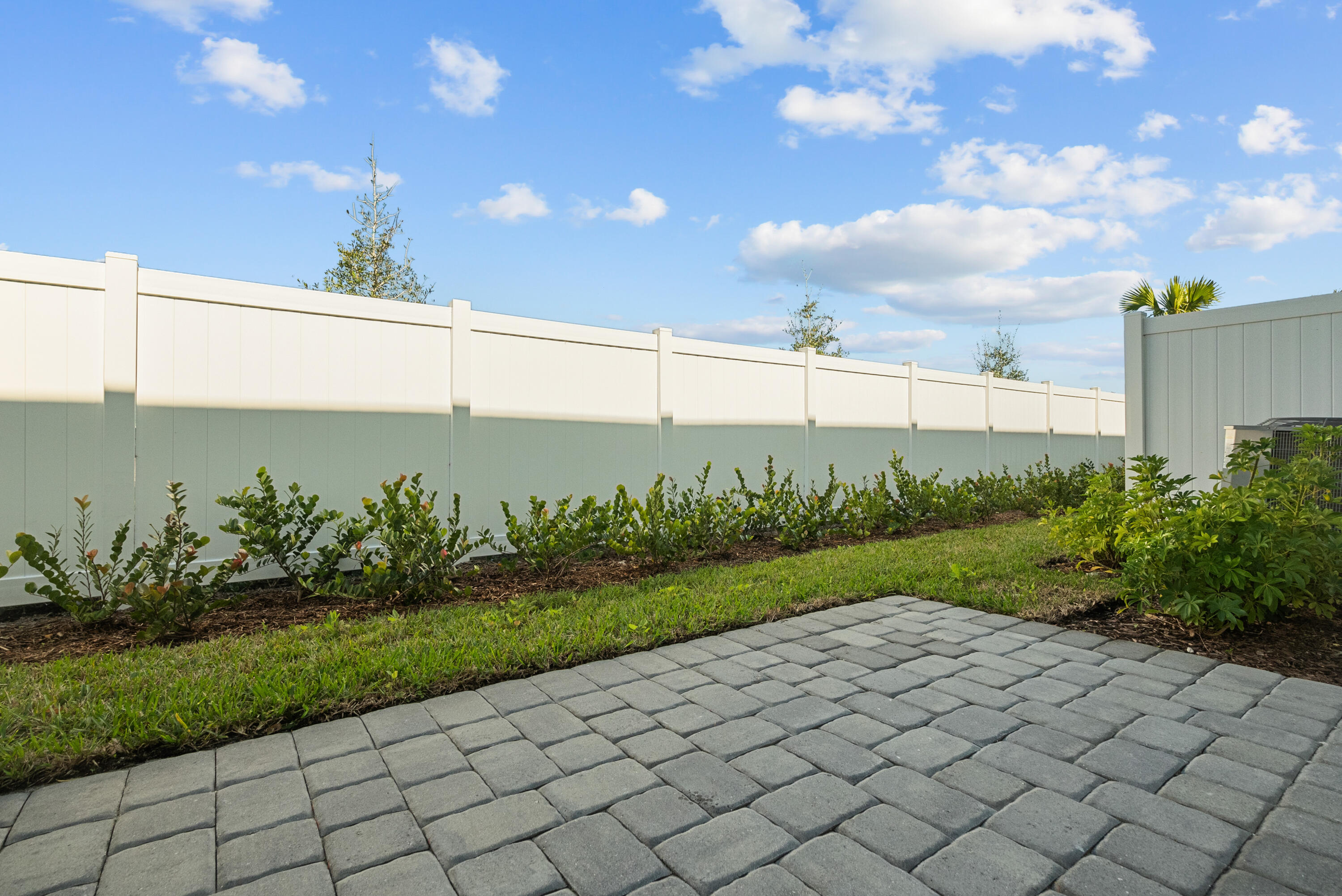 Backyard patio with gray pavers, landscaped lawn, and tall white privacy fence.