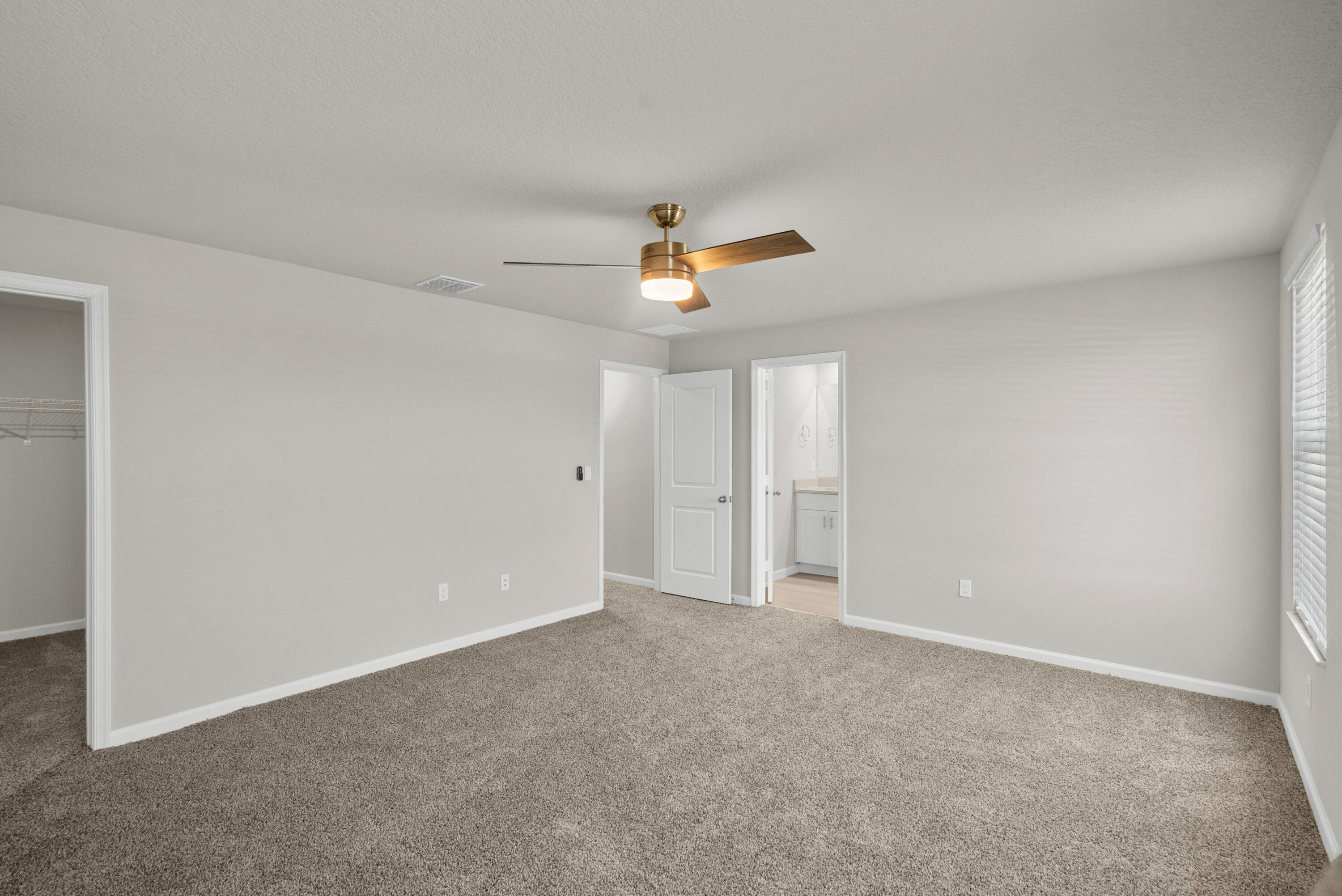 Empty bedroom with beige carpet, a wood-blade ceiling fan, an open closet, and a doorway to the bathroom.