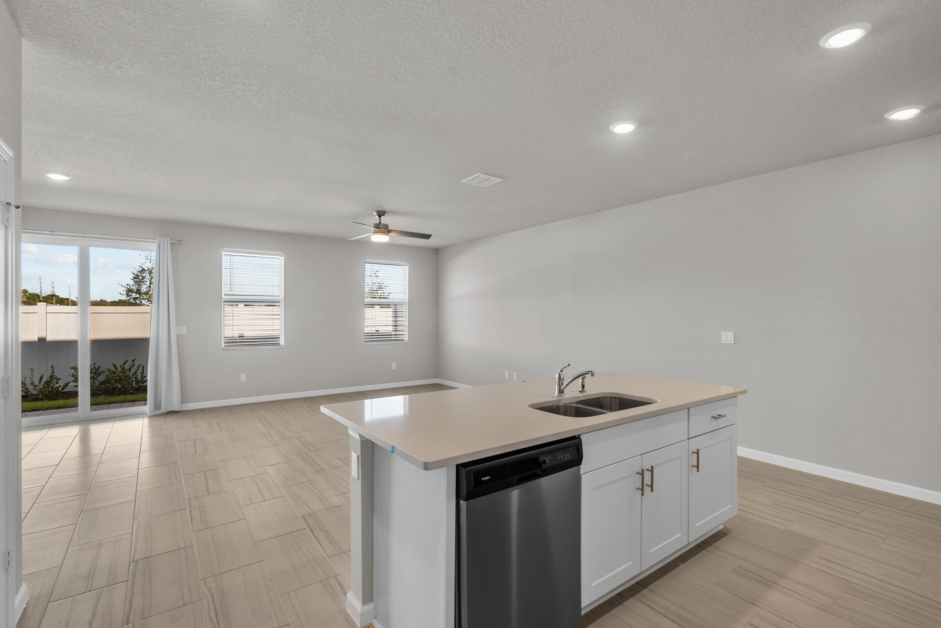 Open-plan kitchen with a white island, stainless-steel dishwasher, tiled floors, and sliding glass doors.
