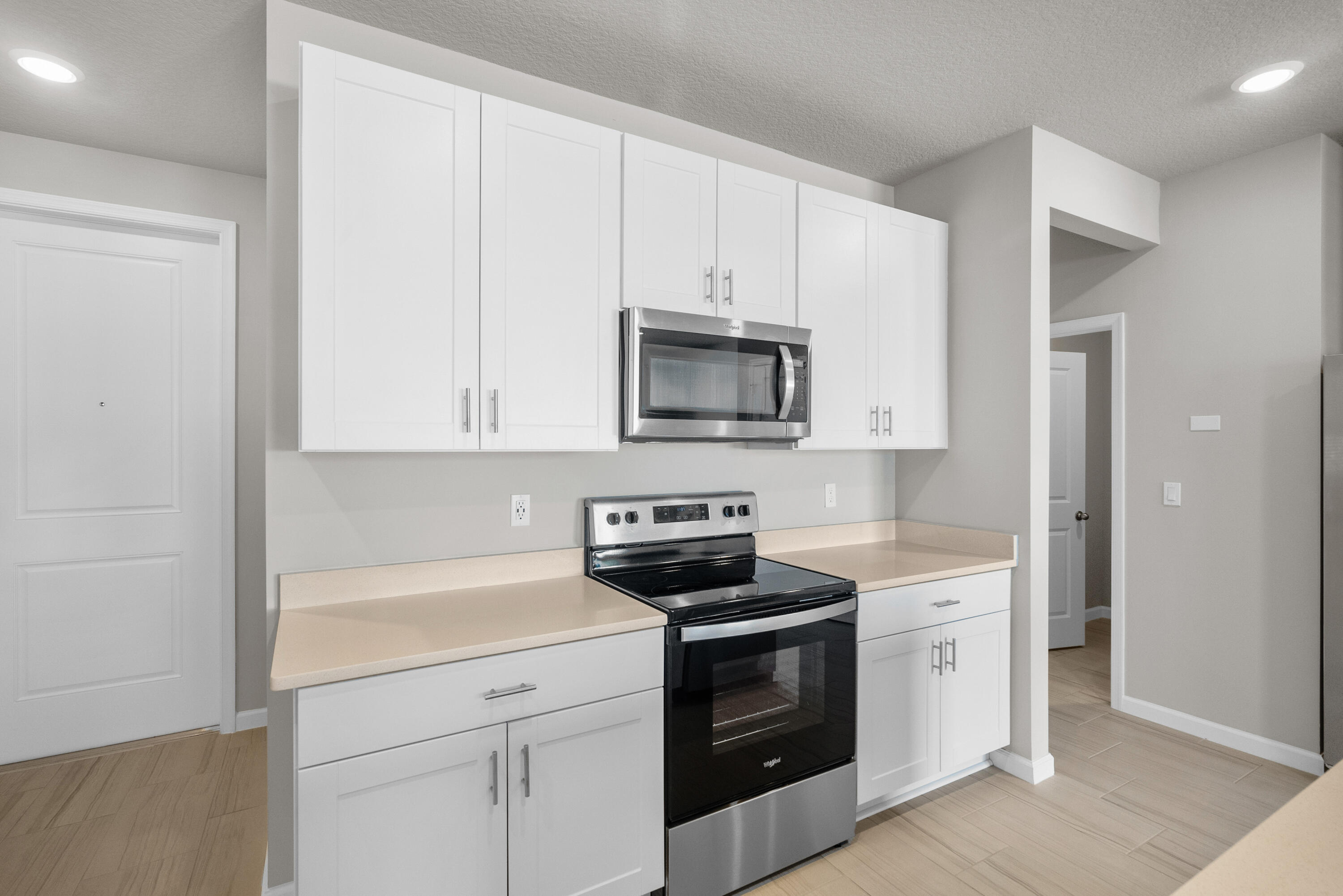 Kitchen with white shaker cabinets, pale counters, and a stainless steel microwave over a black electric range.