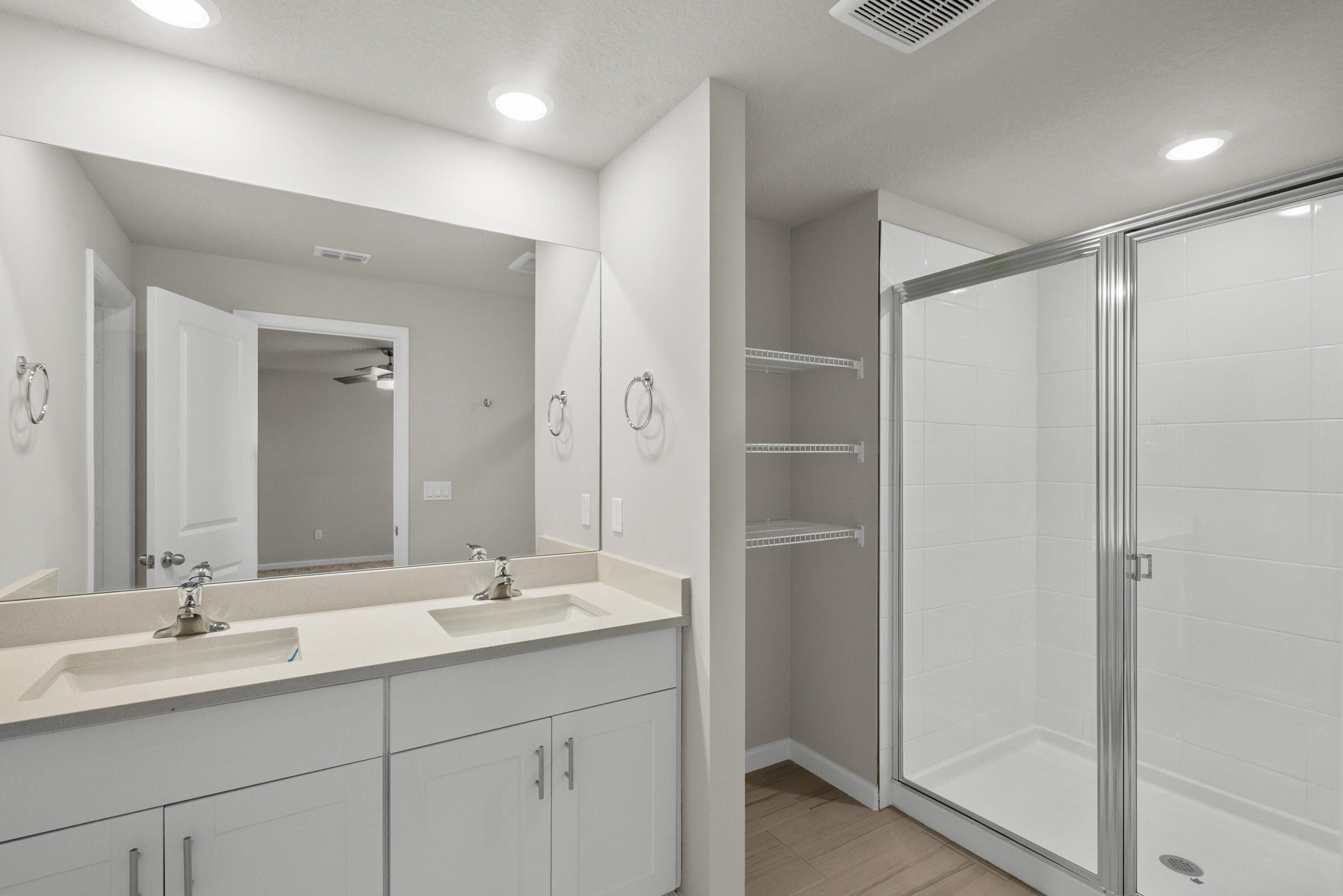 Bathroom with a double-sink vanity, glass-enclosed tiled shower, and open closet shelving.