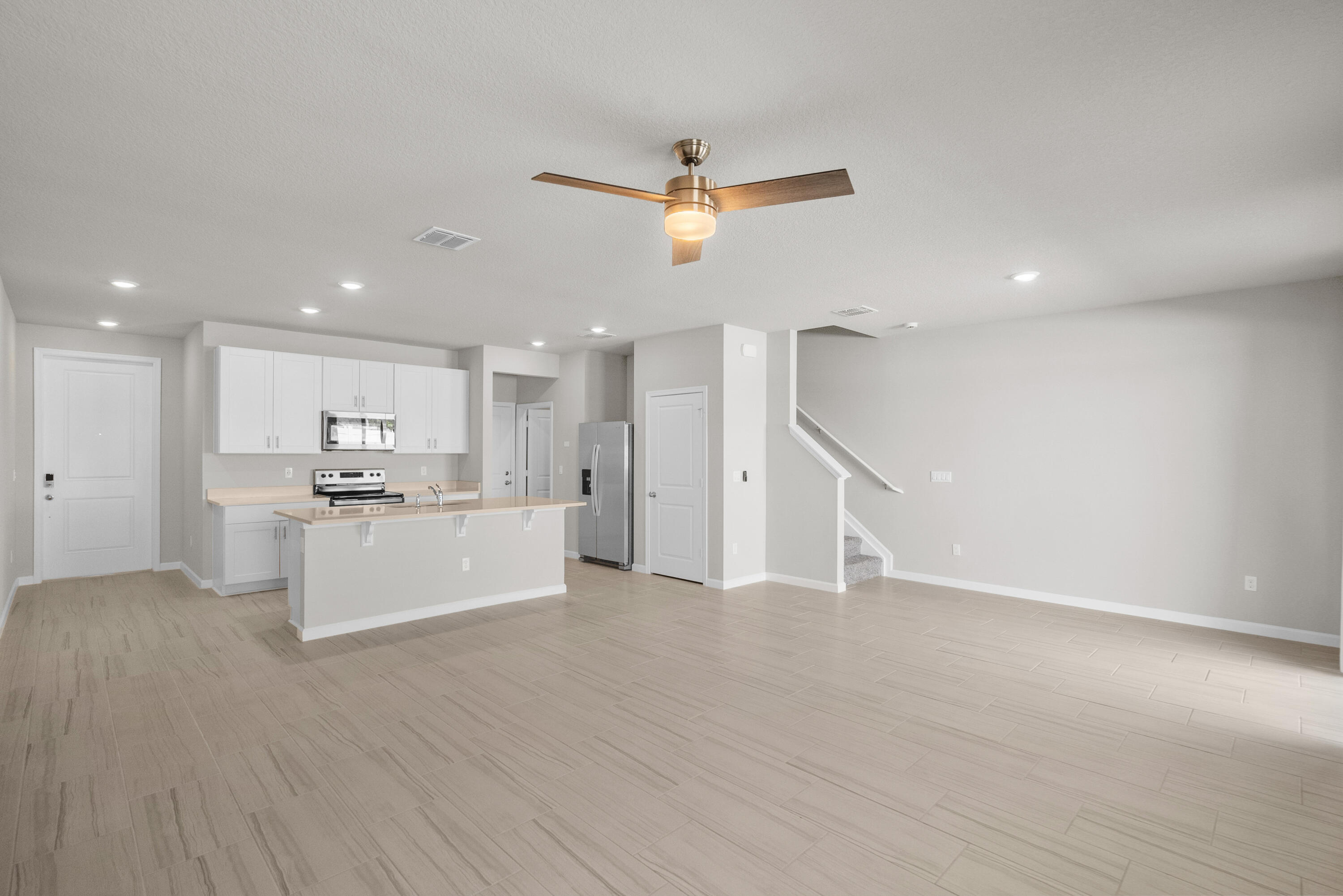 Vacant open-plan kitchen and living area with white cabinets, stainless appliances, tile flooring, and a staircase.