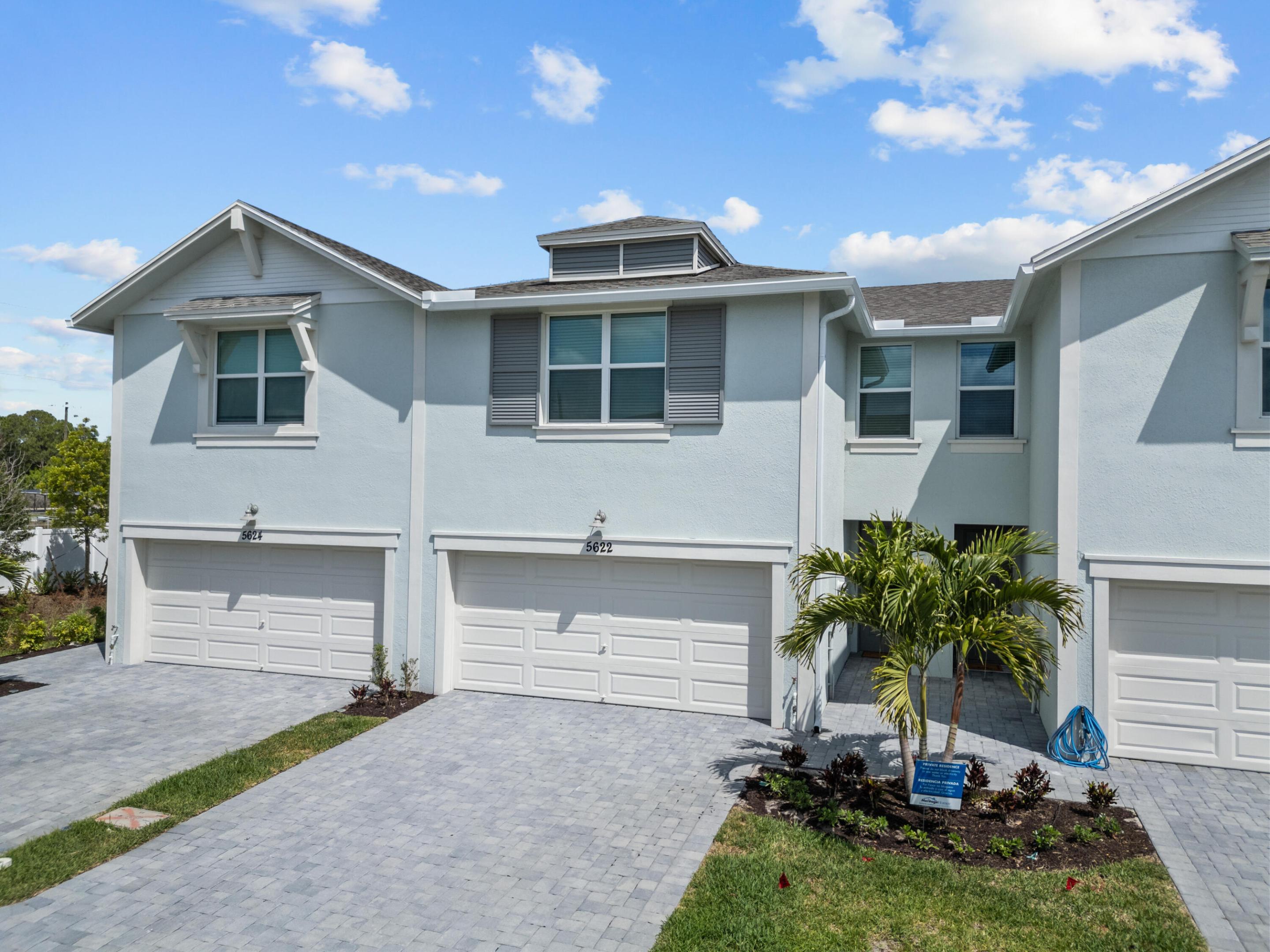 Pale blue attached townhome marked 5622, with a paved driveway and palm trees by the entrance.