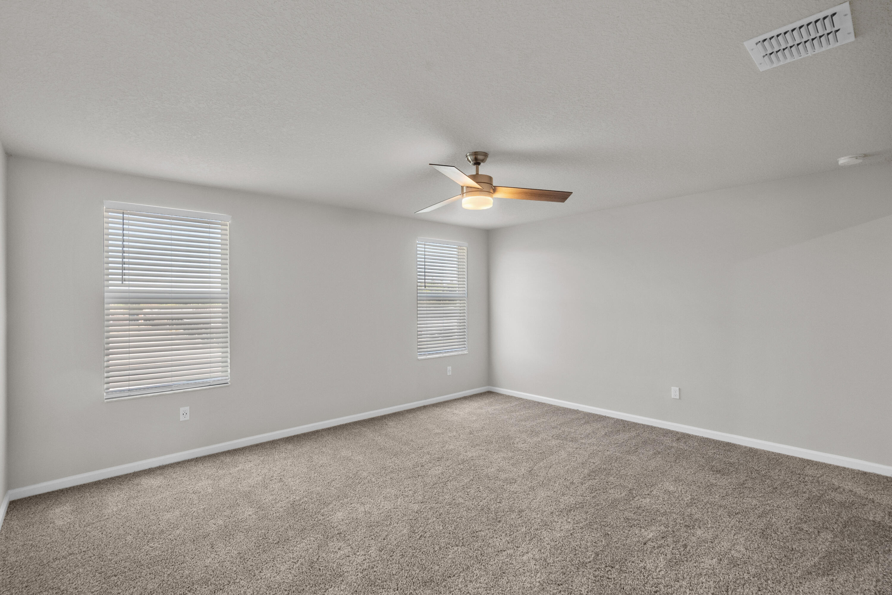 Empty carpeted bedroom with two windows and a ceiling fan with light.