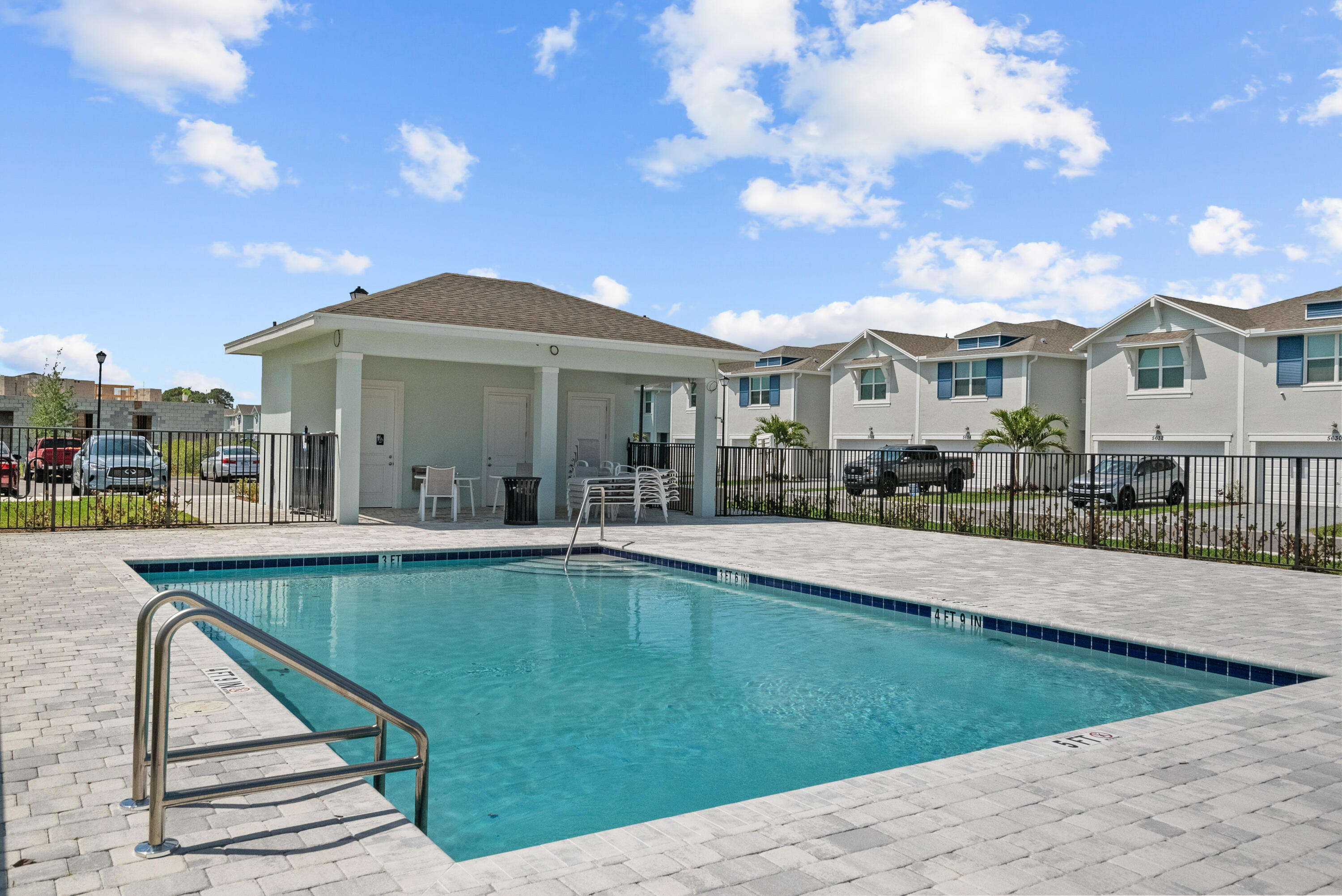 Community pool with a covered seating pavilion and townhomes behind it.