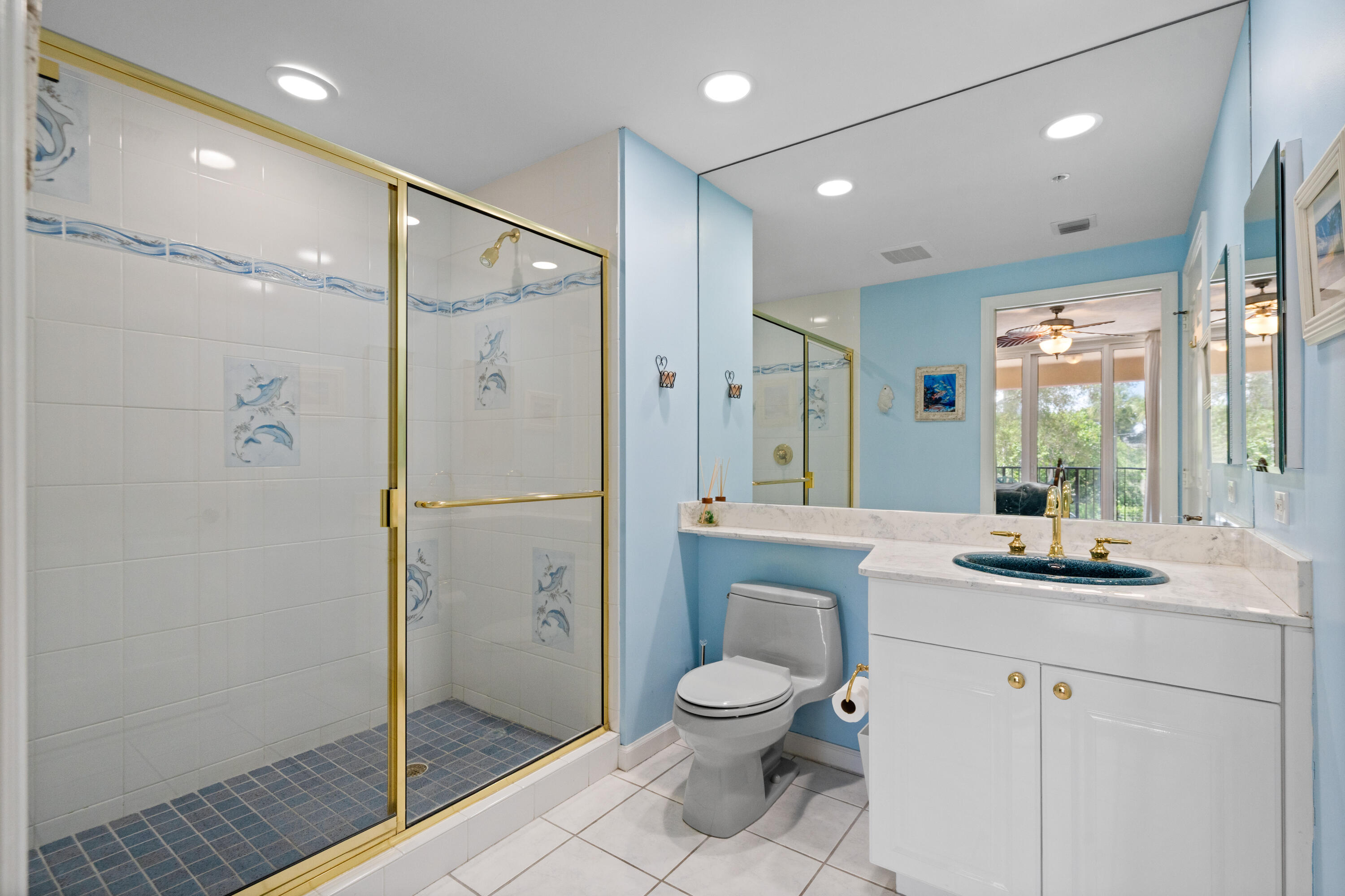 Bathroom with a blue-walled interior, gold-trimmed shower, and white vanity with blue sink.