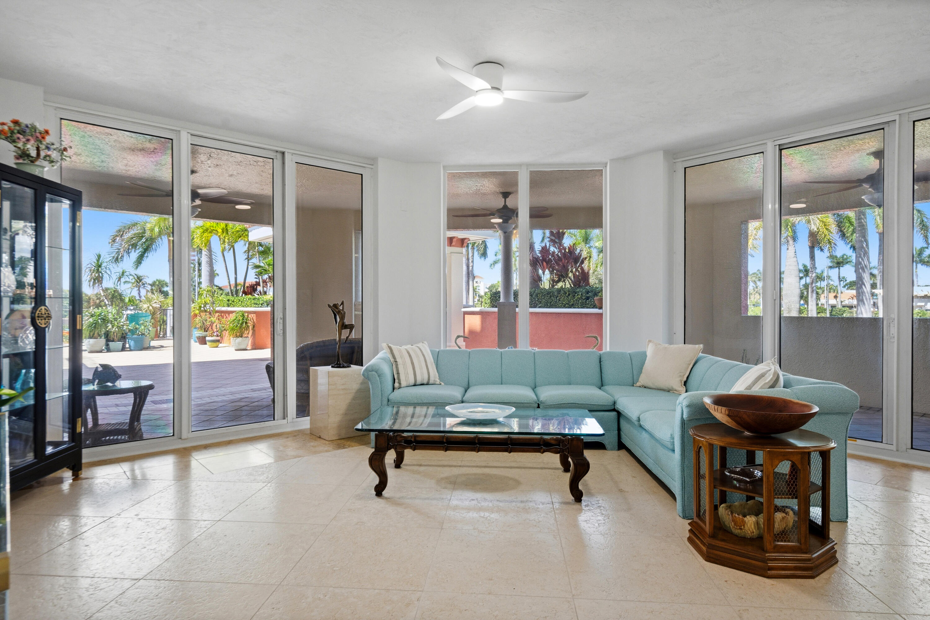 Living room with a turquoise sectional and floor-to-ceiling doors opening onto a palm-lined patio.
