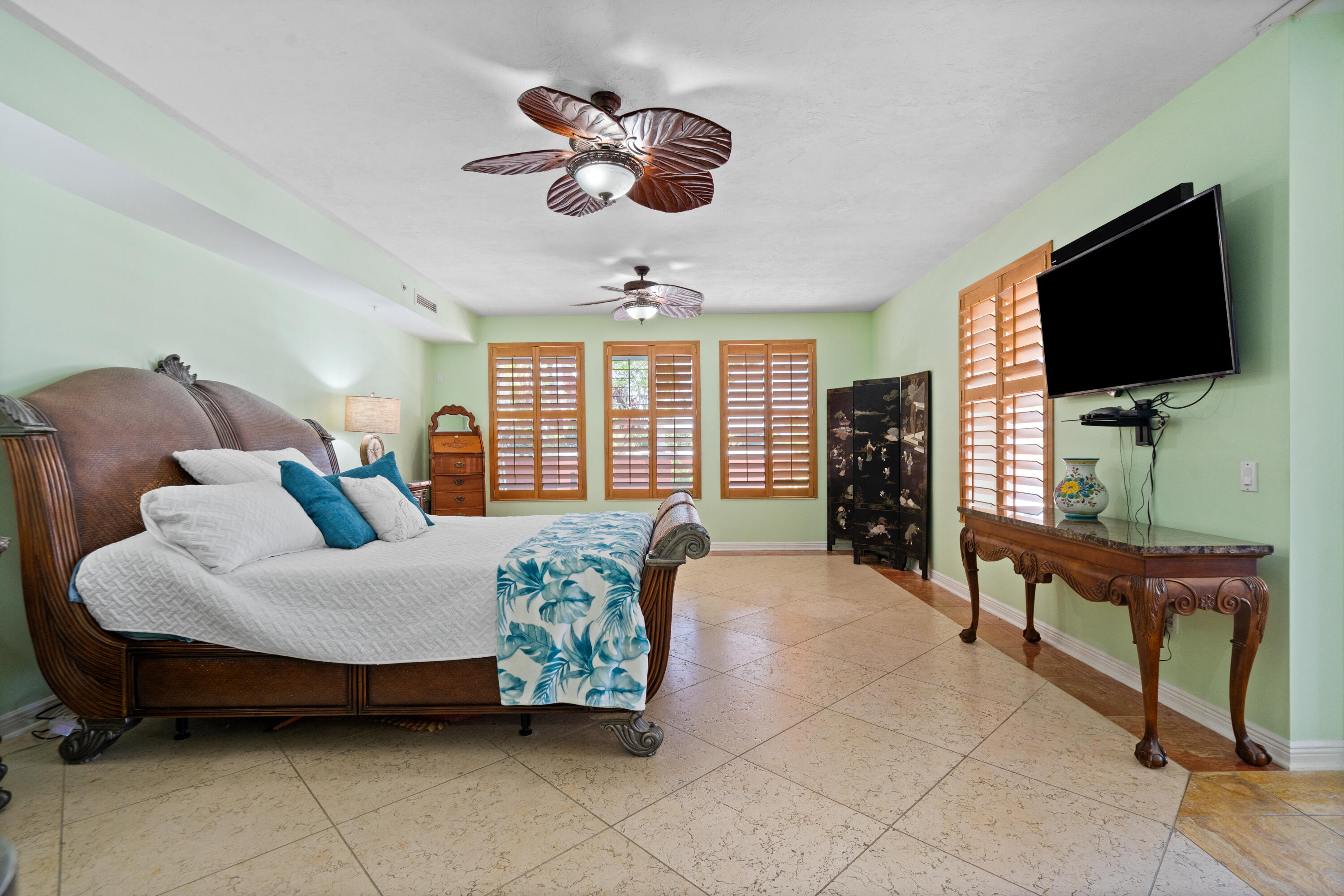 Bedroom with a carved wooden bed, blue floral throw, plantation shutters, and wall-mounted television.