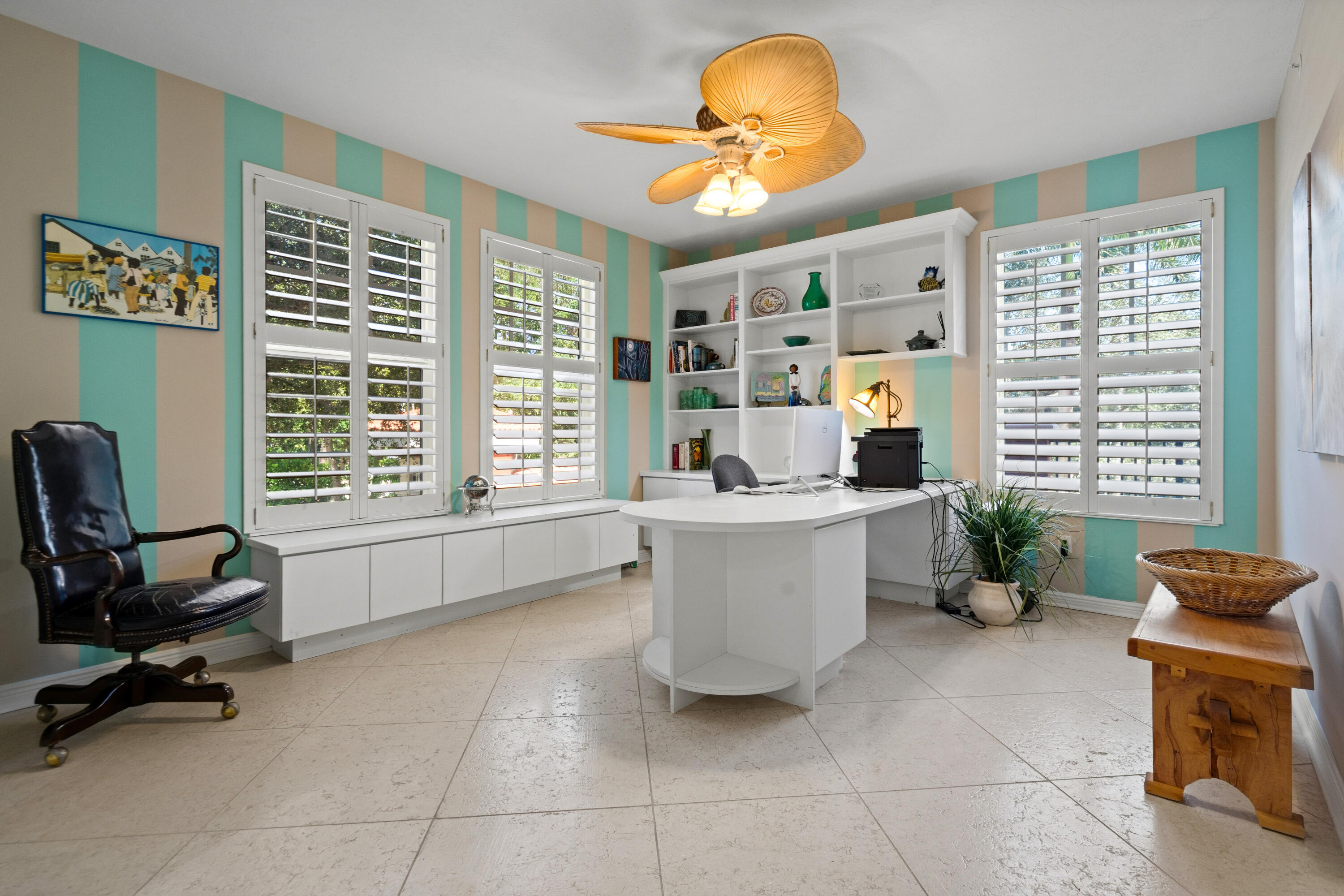 Home office with striped walls, plantation shutters, built-in shelves, and a curved white desk.