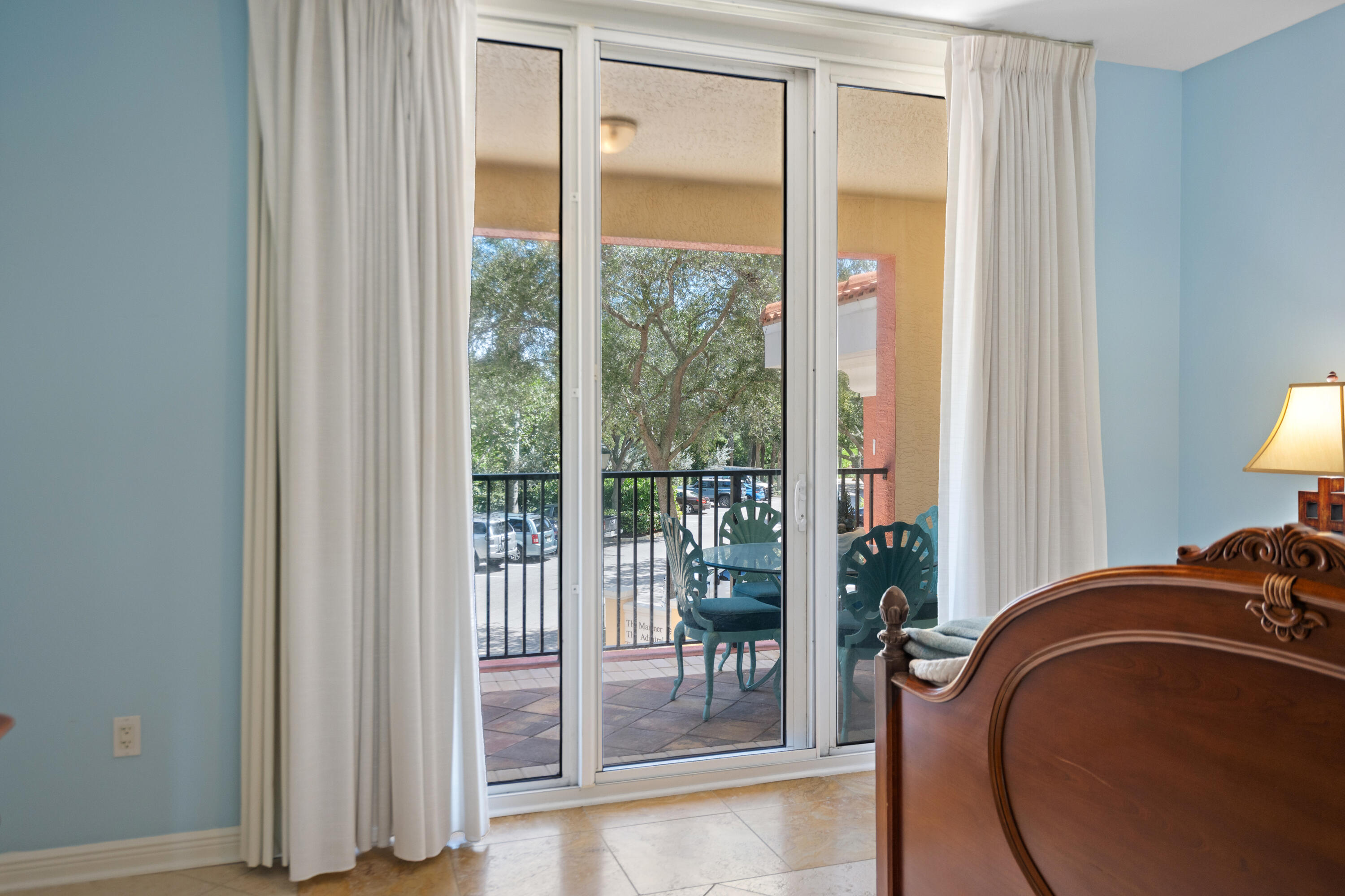 Furnished bedroom with sliding glass doors opening to a tiled patio with teal chairs.