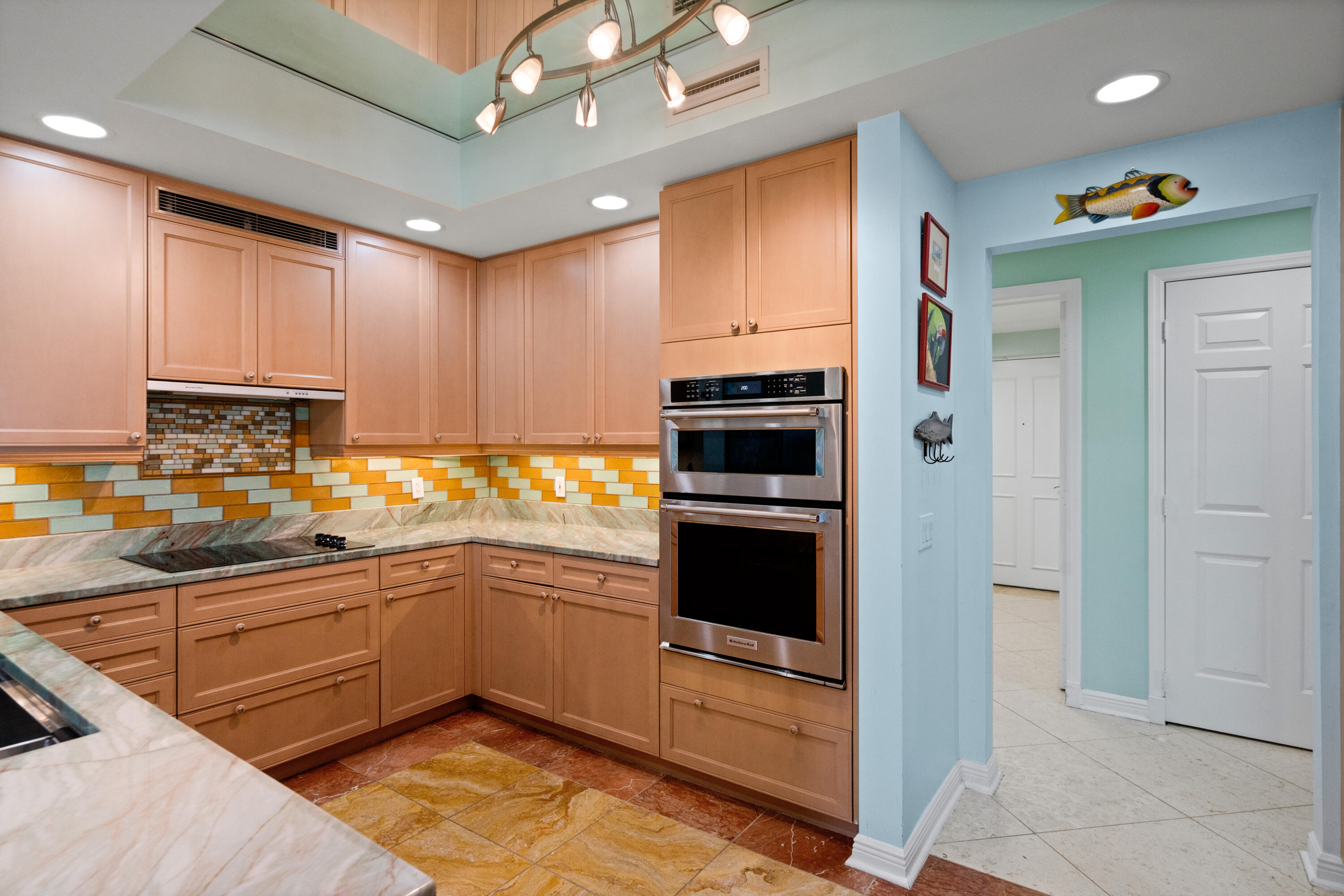 Kitchen with warm wood cabinets, colorful tile backsplash, stone counters, and stainless steel double ovens.