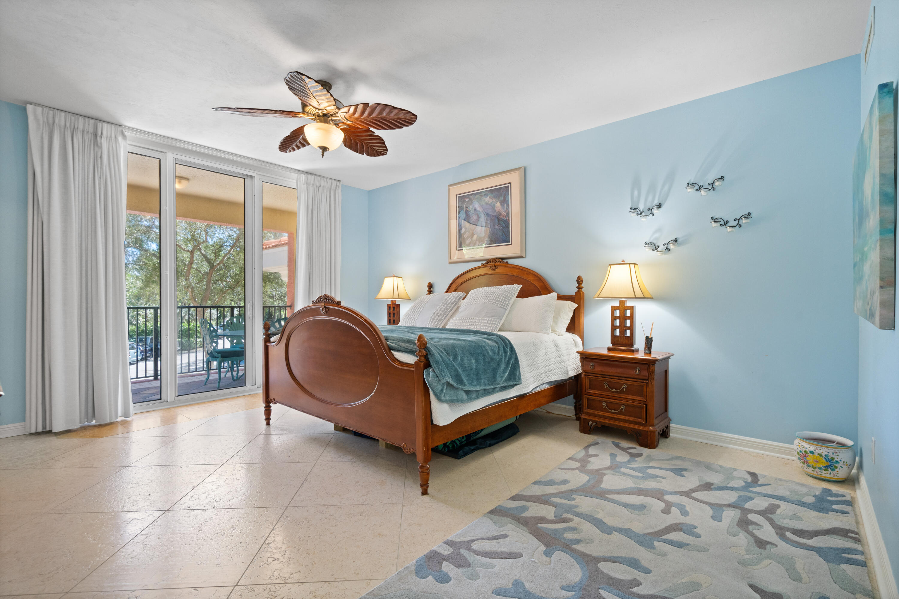 Furnished bedroom with a wooden bed, blue walls, and sliding glass doors opening to a balcony.