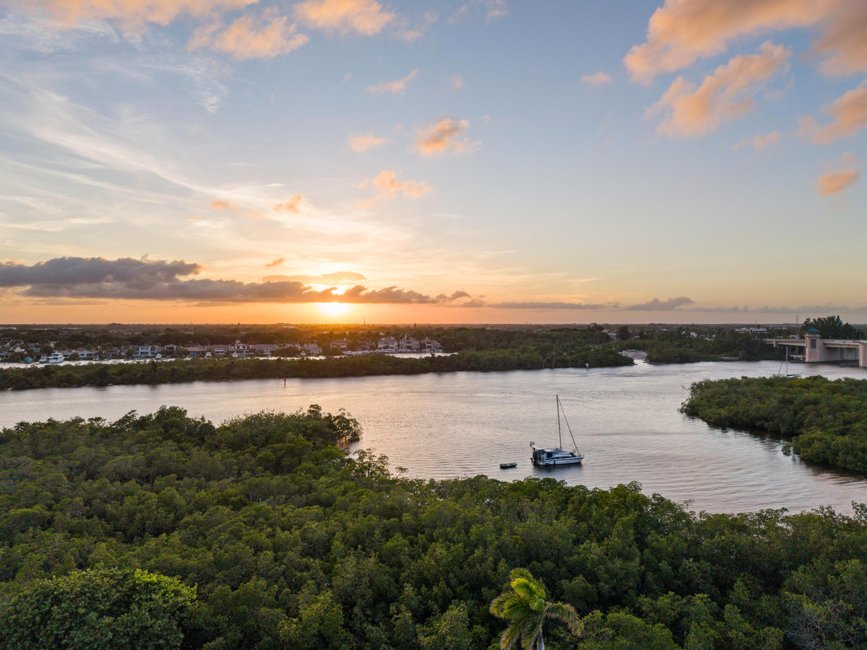 Aerial view of a winding waterway at sunset, with mangroves and a sailboat.