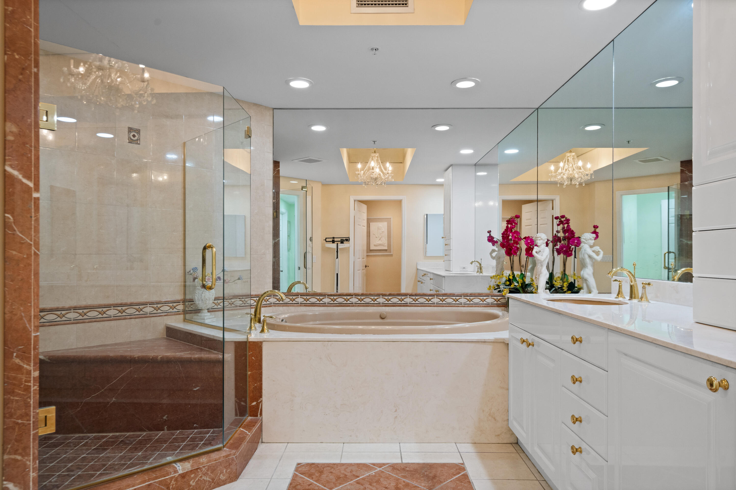 Bathroom with a glass shower, oval soaking tub, and white vanity topped with magenta orchids.