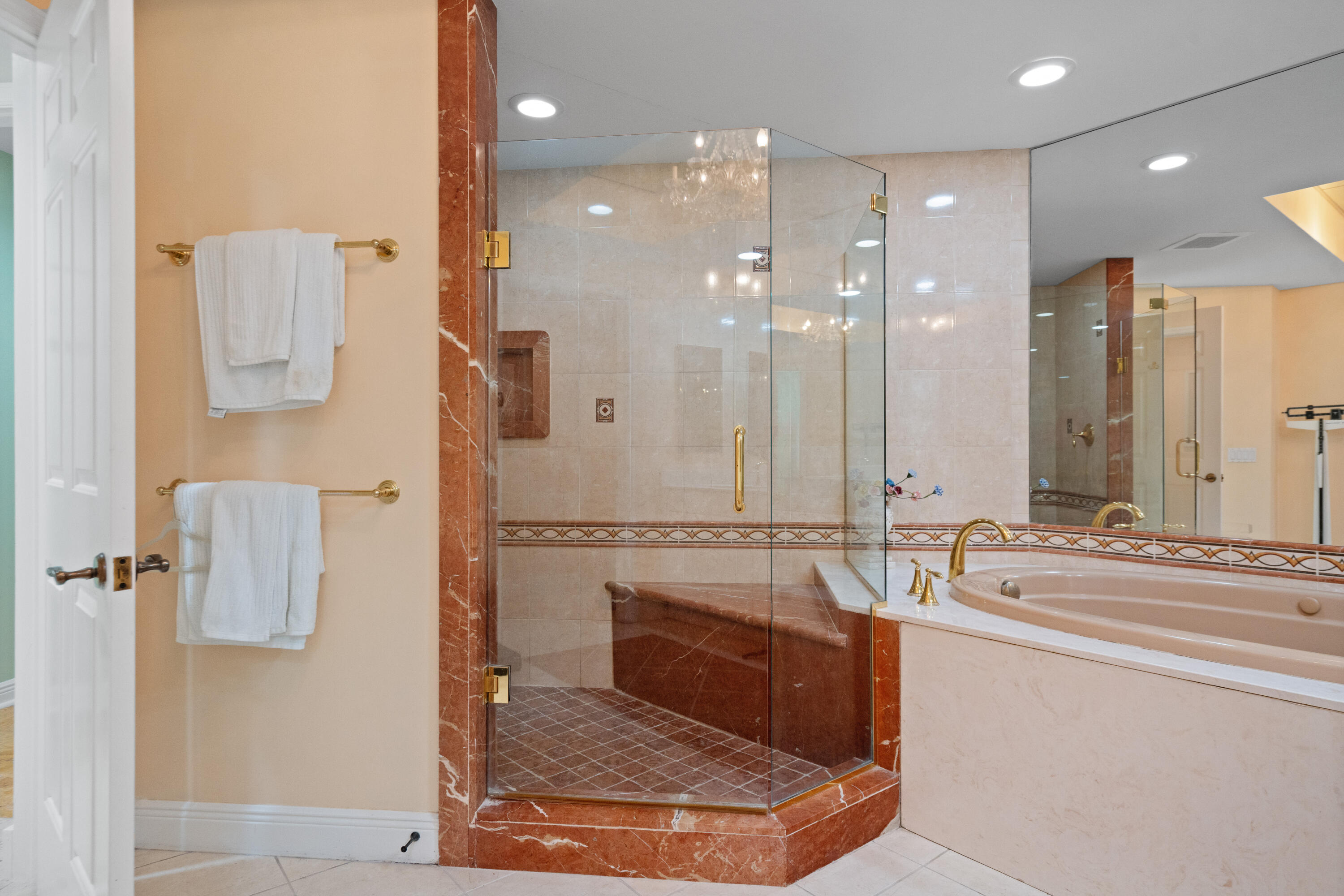 Bathroom with a glass-enclosed shower, reddish marble trim, built-in bench, and jetted bathtub.
