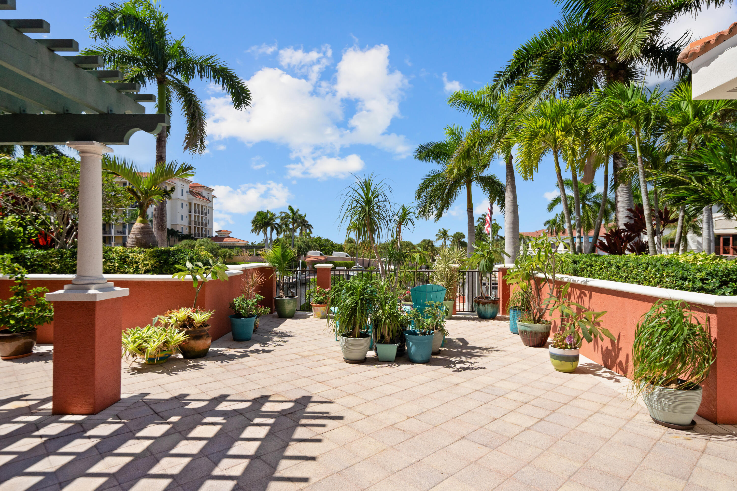 Outdoor terrace with potted tropical plants, coral-colored walls, and a teal chair.