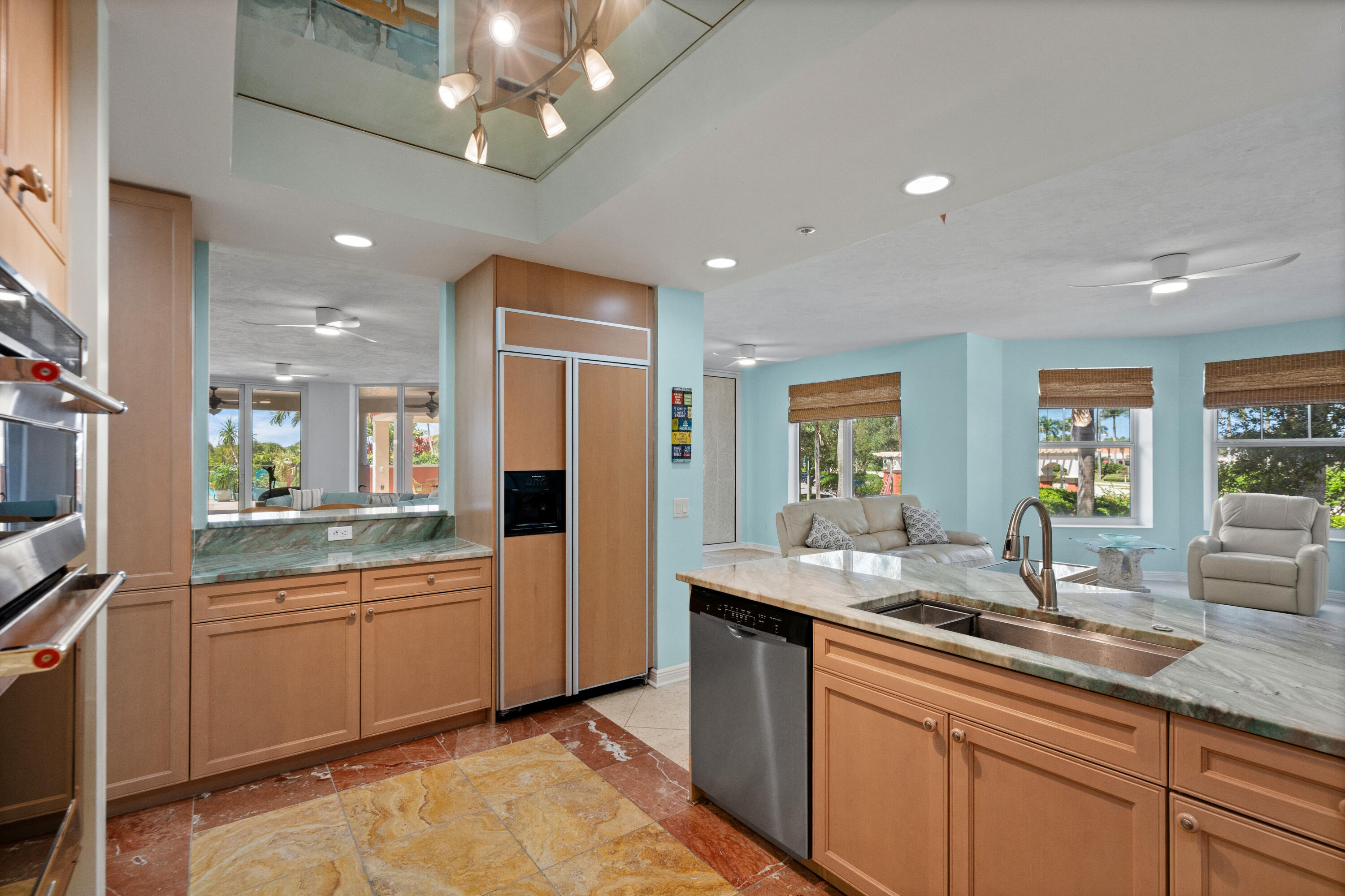 Open kitchen with a stone island, warm wood cabinets, stainless appliances, and an adjoining living area.