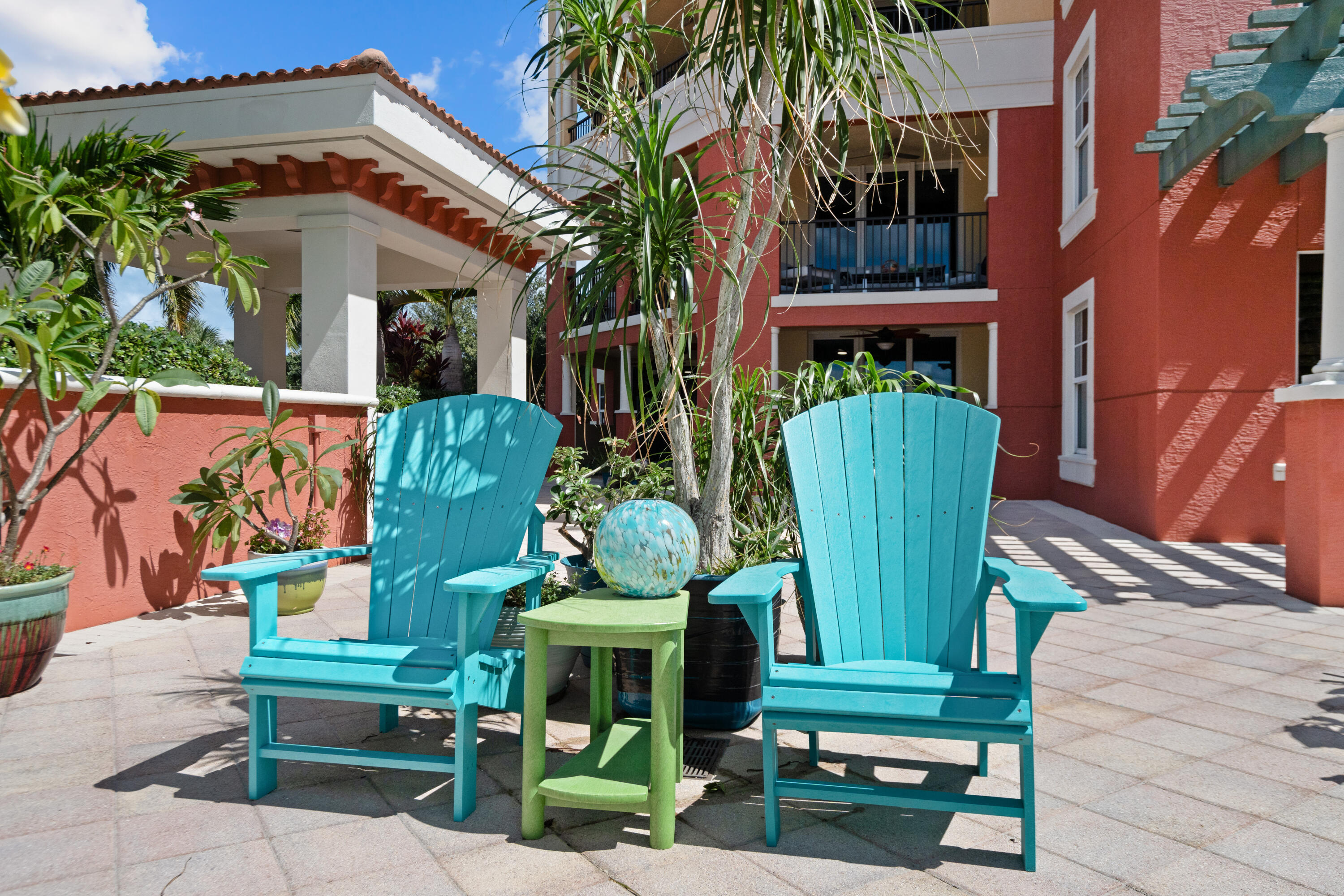 Condominium courtyard with turquoise Adirondack chairs, a green table, and tropical plants.