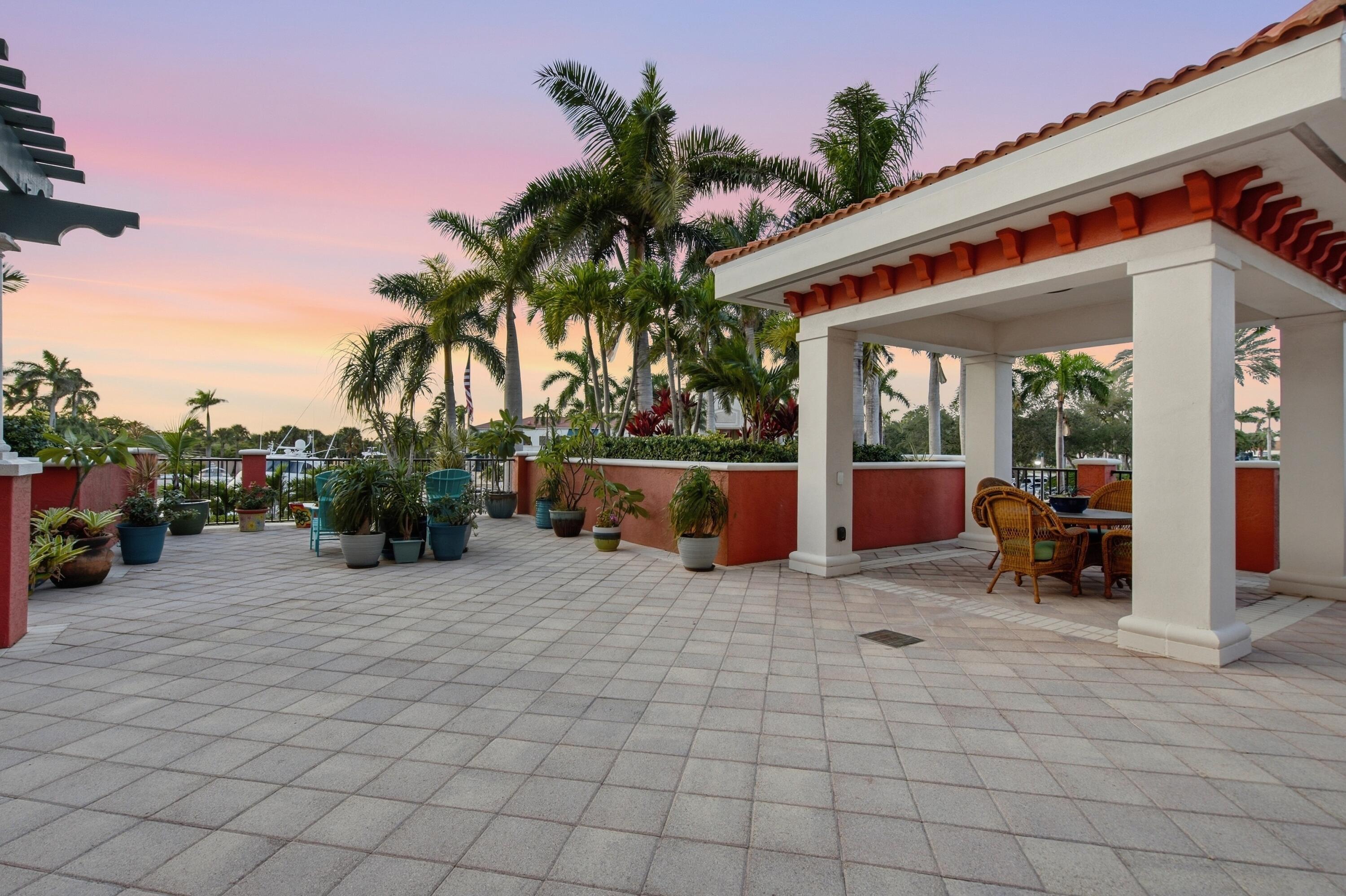 Tiled terrace with a covered wicker dining area and palm trees at sunset.