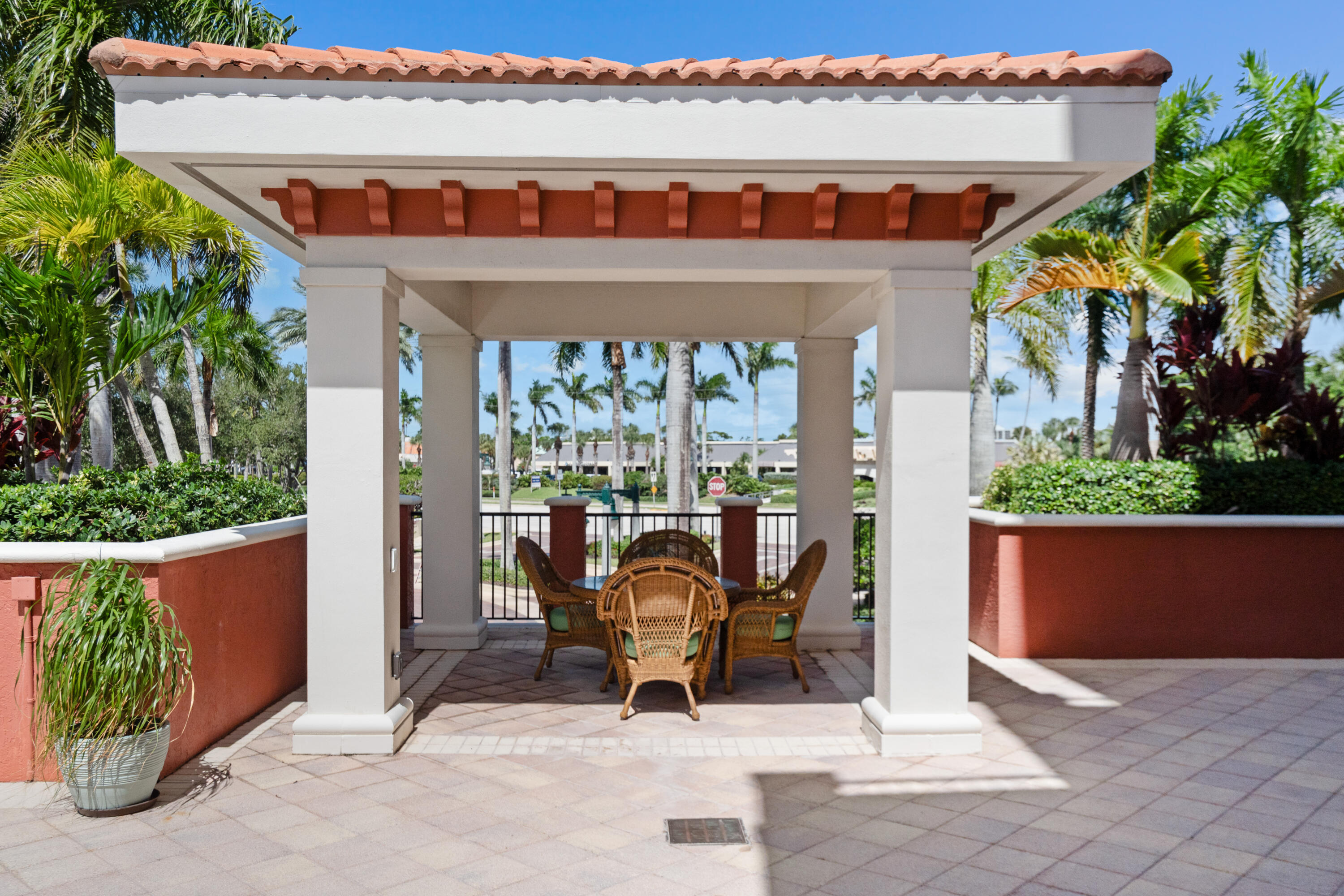 Covered patio with wicker dining set, tiled floor, and tropical landscaping.