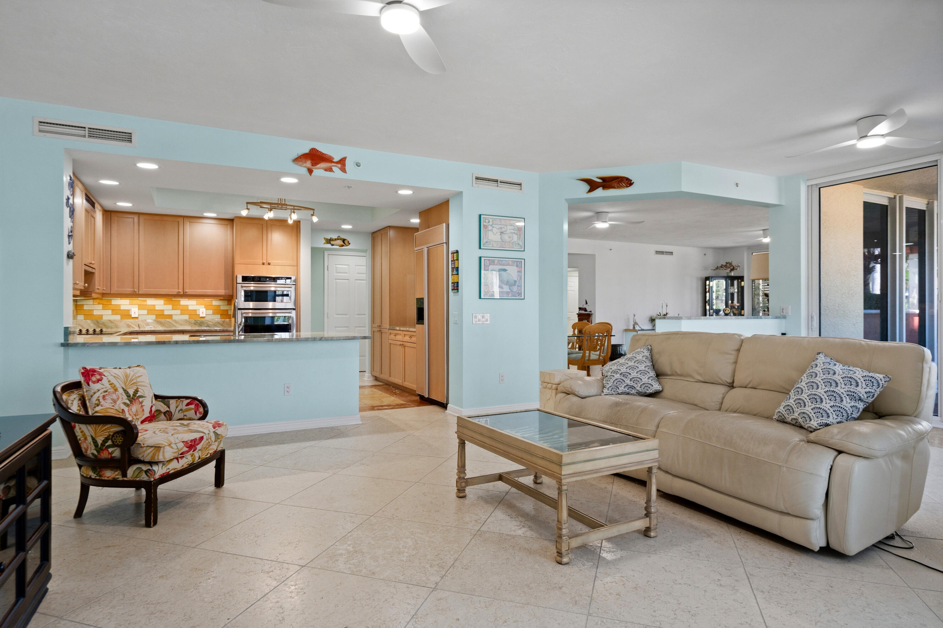 Open-plan living room with beige sofa and floral armchair beside a wood-cabinet kitchen.