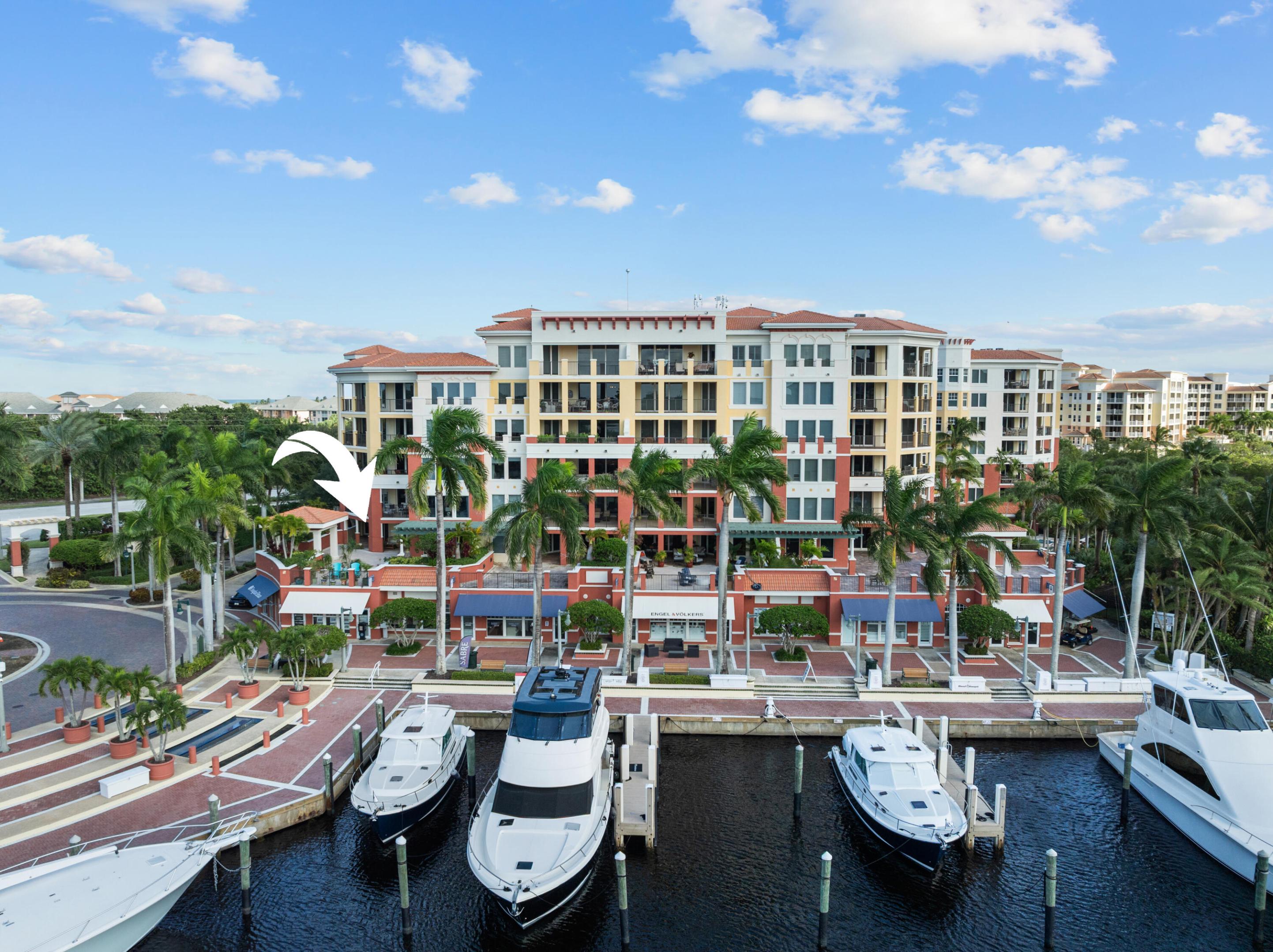 Waterfront condominium complex with marina and boats; a white arrow points toward the building.