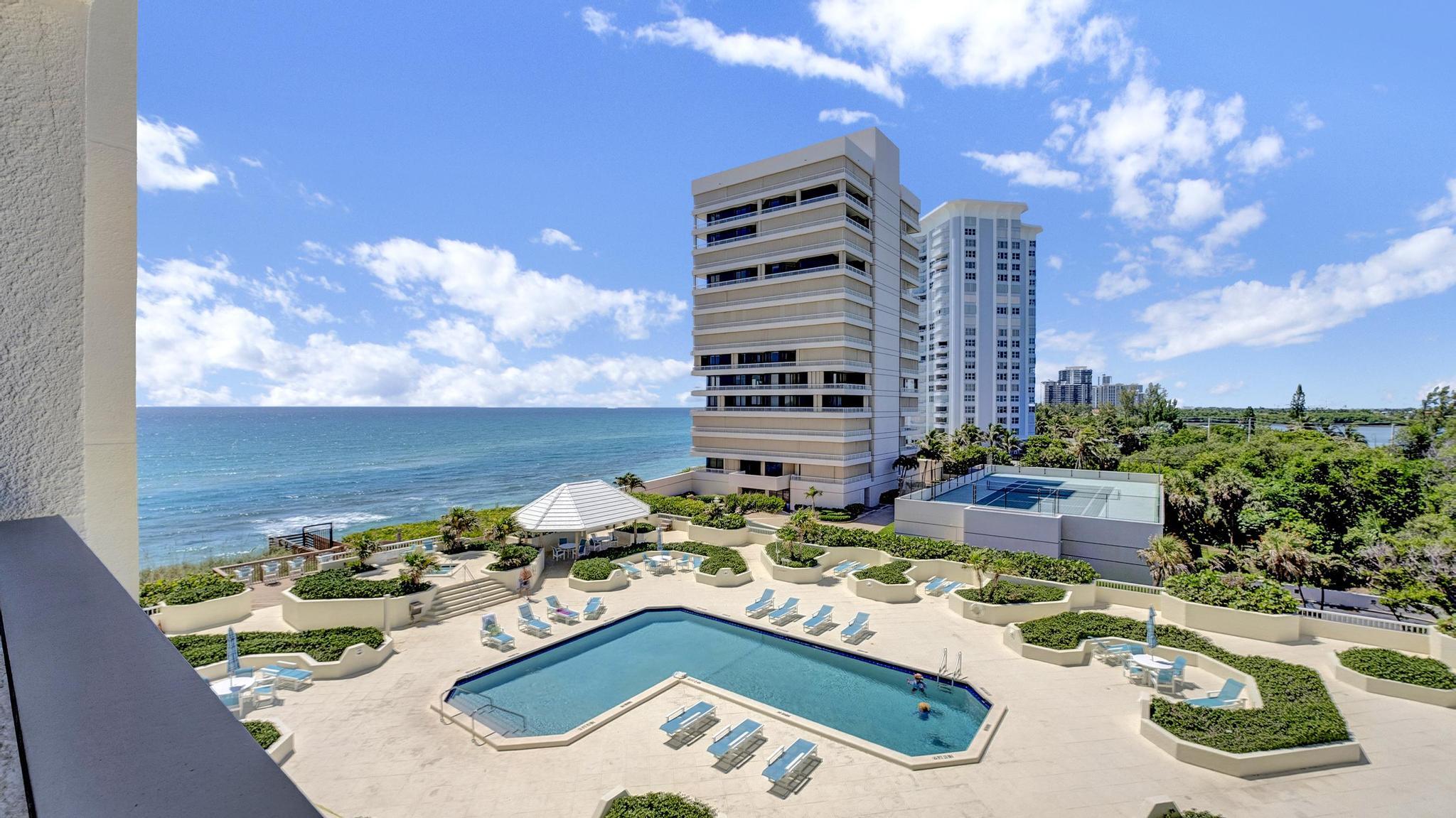 Oceanfront condominium pool deck with high-rise buildings, tennis court, and Atlantic Ocean view.