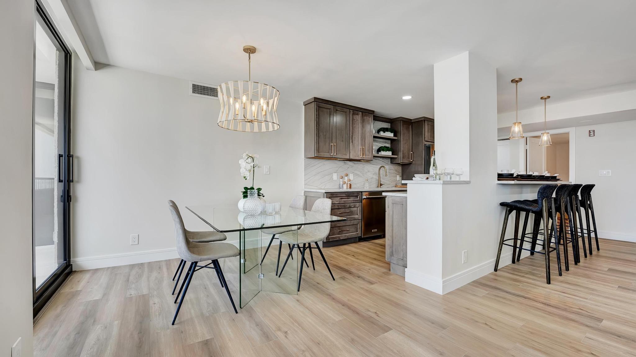 Open-plan kitchen and dining area with dark cabinets, glass table, and breakfast bar.