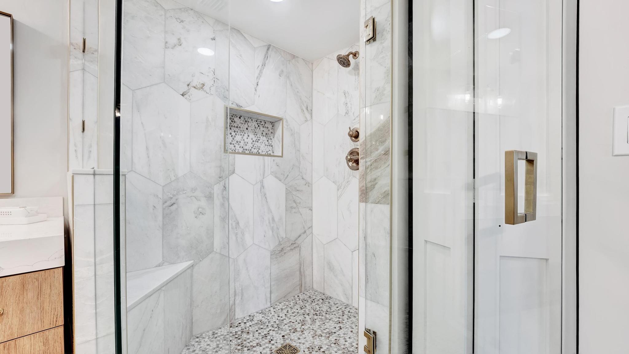Glass-enclosed marble-look shower with a pebble floor, recessed niche, and brass fixtures.