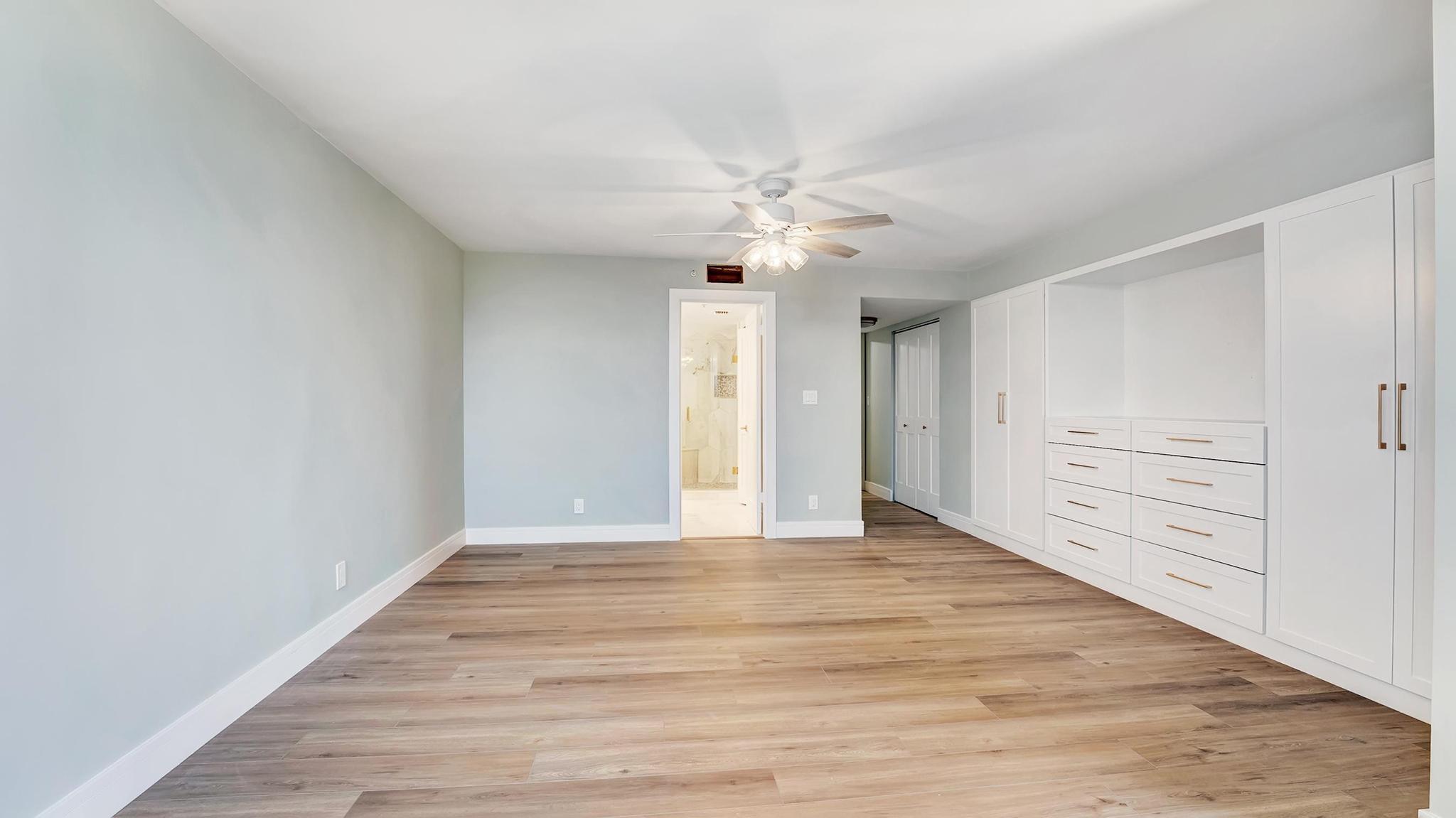 Empty bedroom with white built-in wardrobes, wood-look flooring, and a ceiling fan.