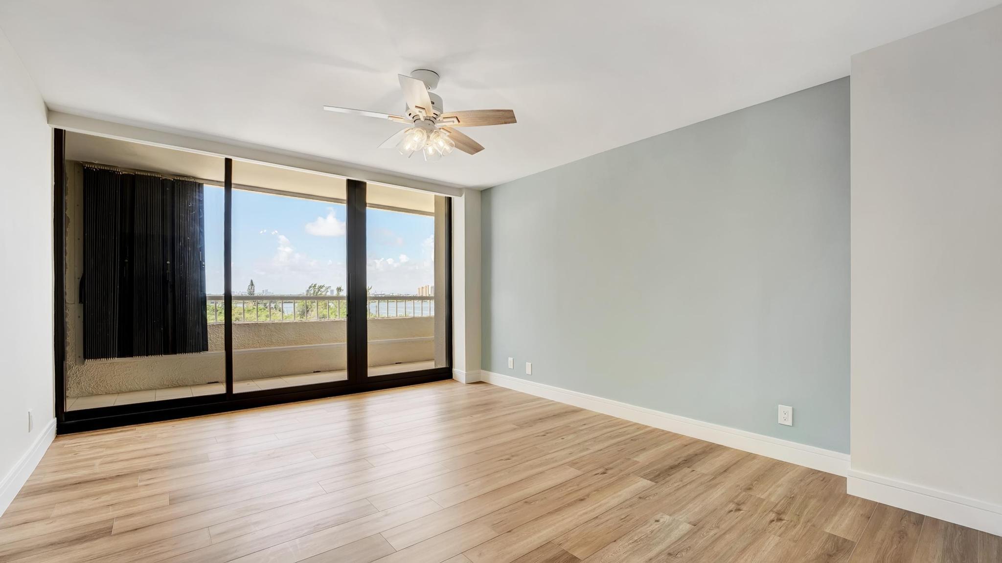 Empty room with light wood-look floors and sliding doors opening to a balcony overlooking water.