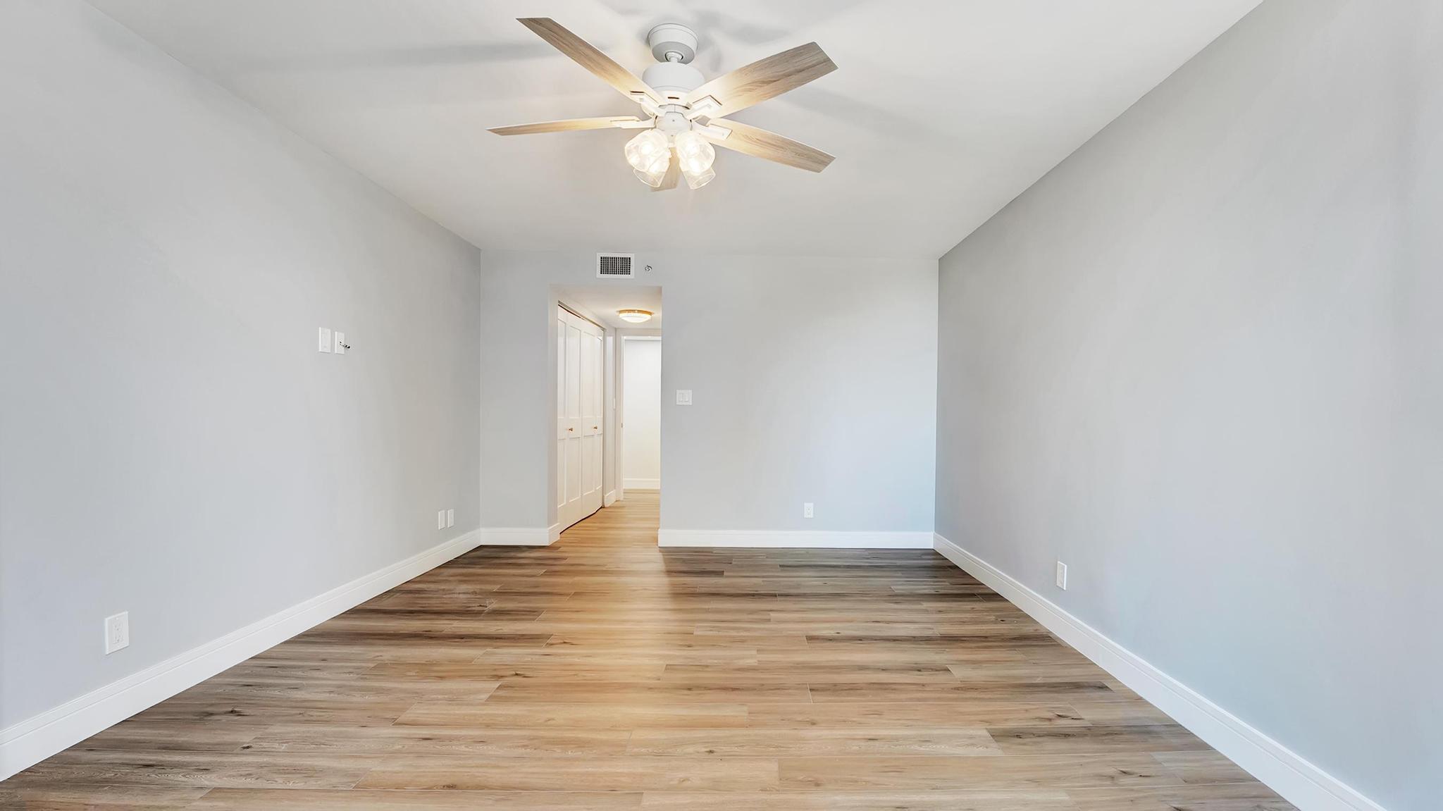 Empty bedroom with wood-look floors, gray walls, and a ceiling fan with lights.