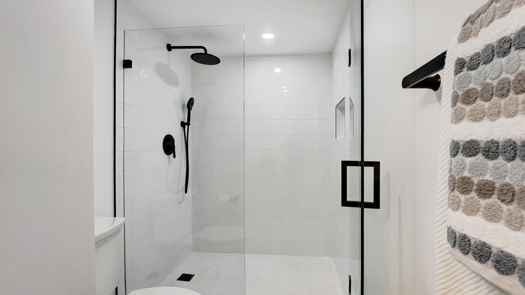 Walk-in shower with white tile, black fixtures, and a patterned towel.