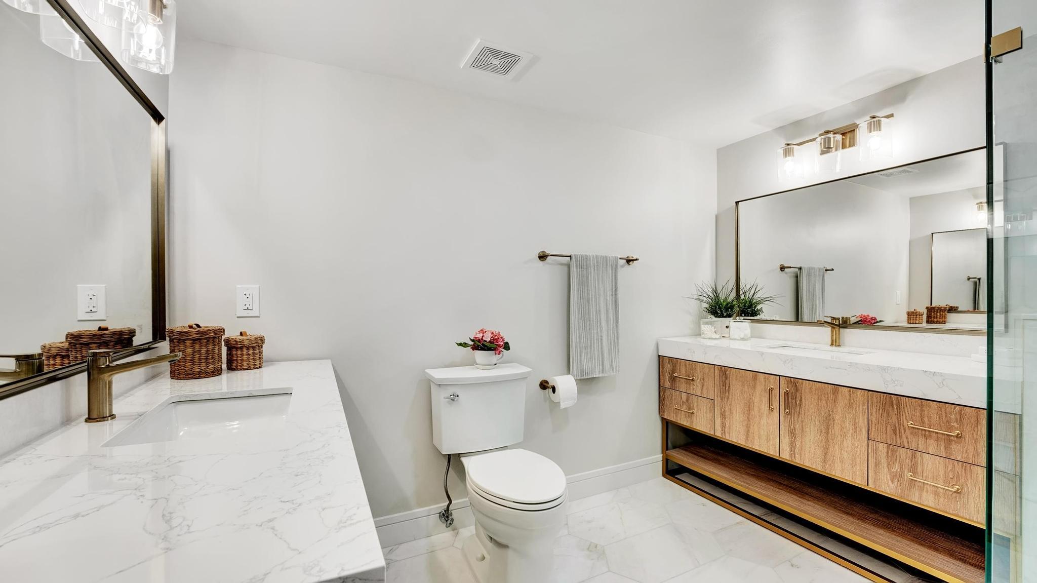Modern bathroom with a wood-front vanity, marble-look counters, large mirrors, and glass shower.