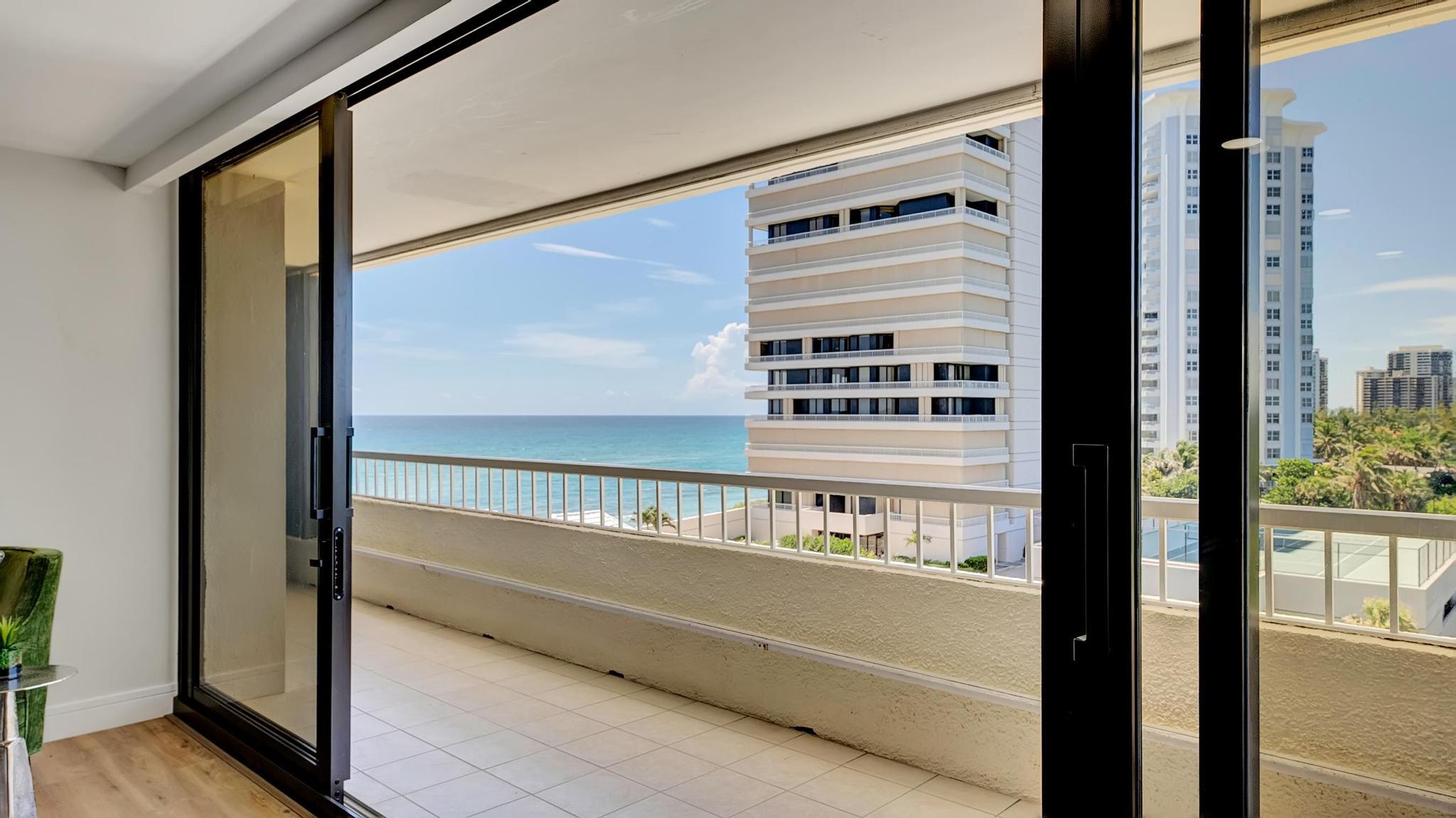 Apartment balcony with ocean views, tiled floor, and neighboring high-rise buildings.