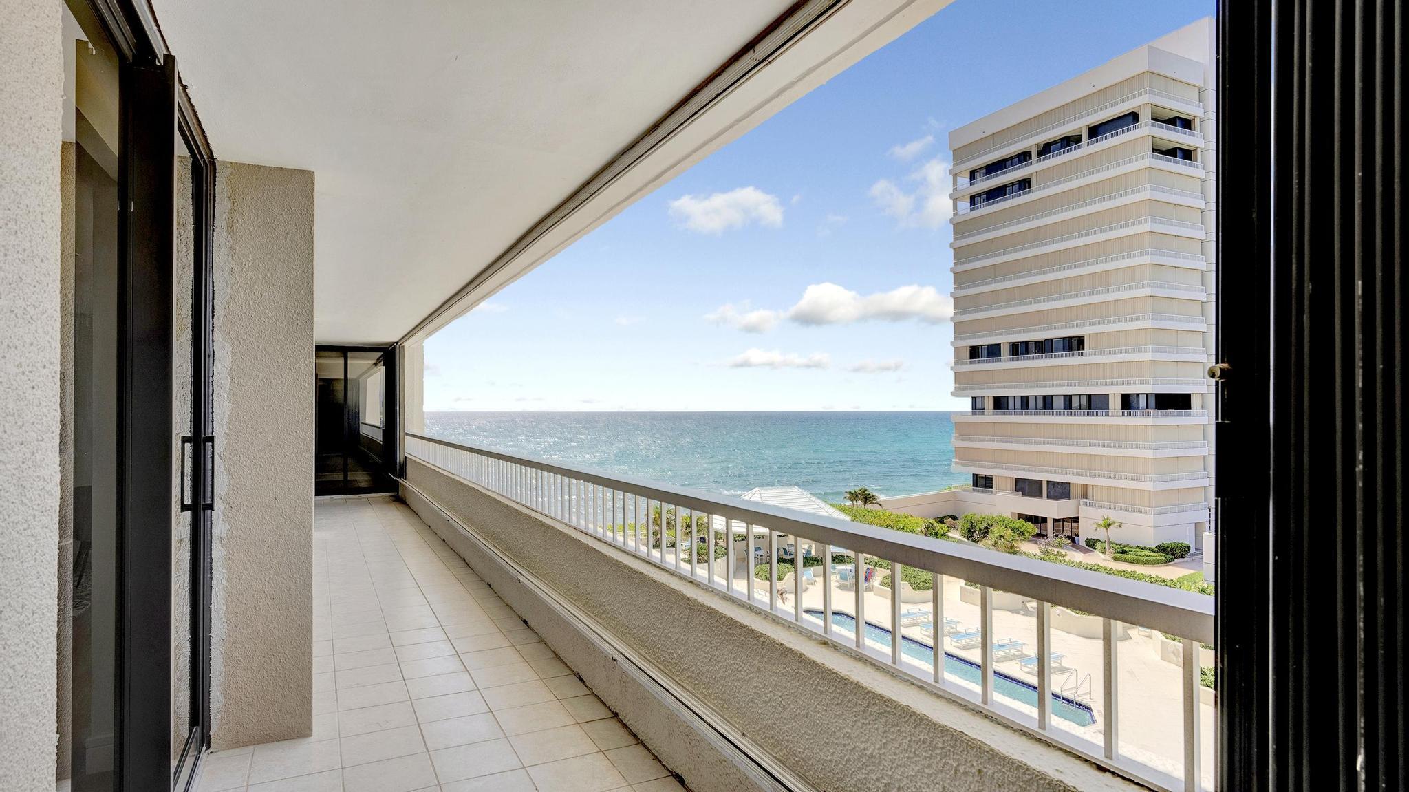 Condominium balcony overlooking the ocean, with a neighboring high-rise and pool below.