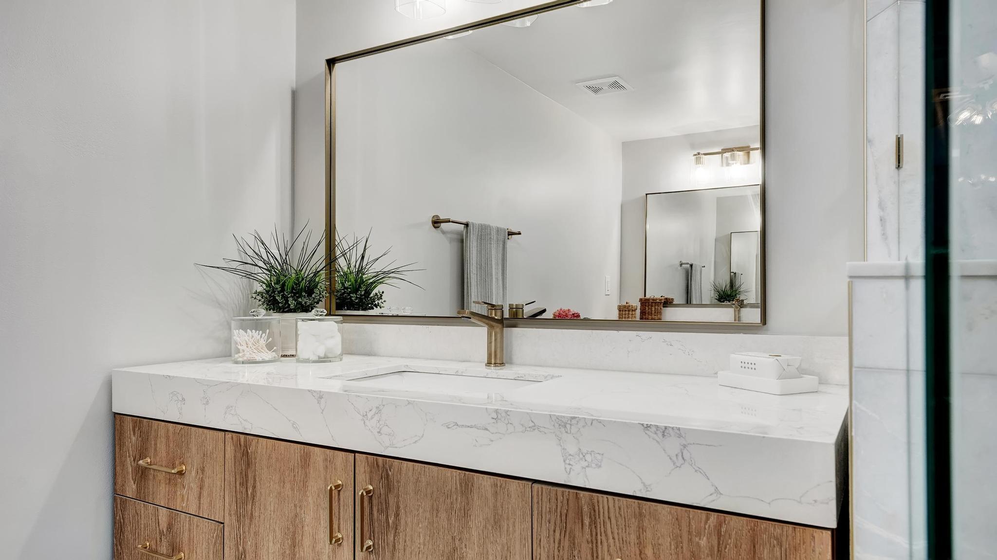 Bathroom vanity with a veined stone counter, wood cabinets, brass fixtures, and a large mirror.