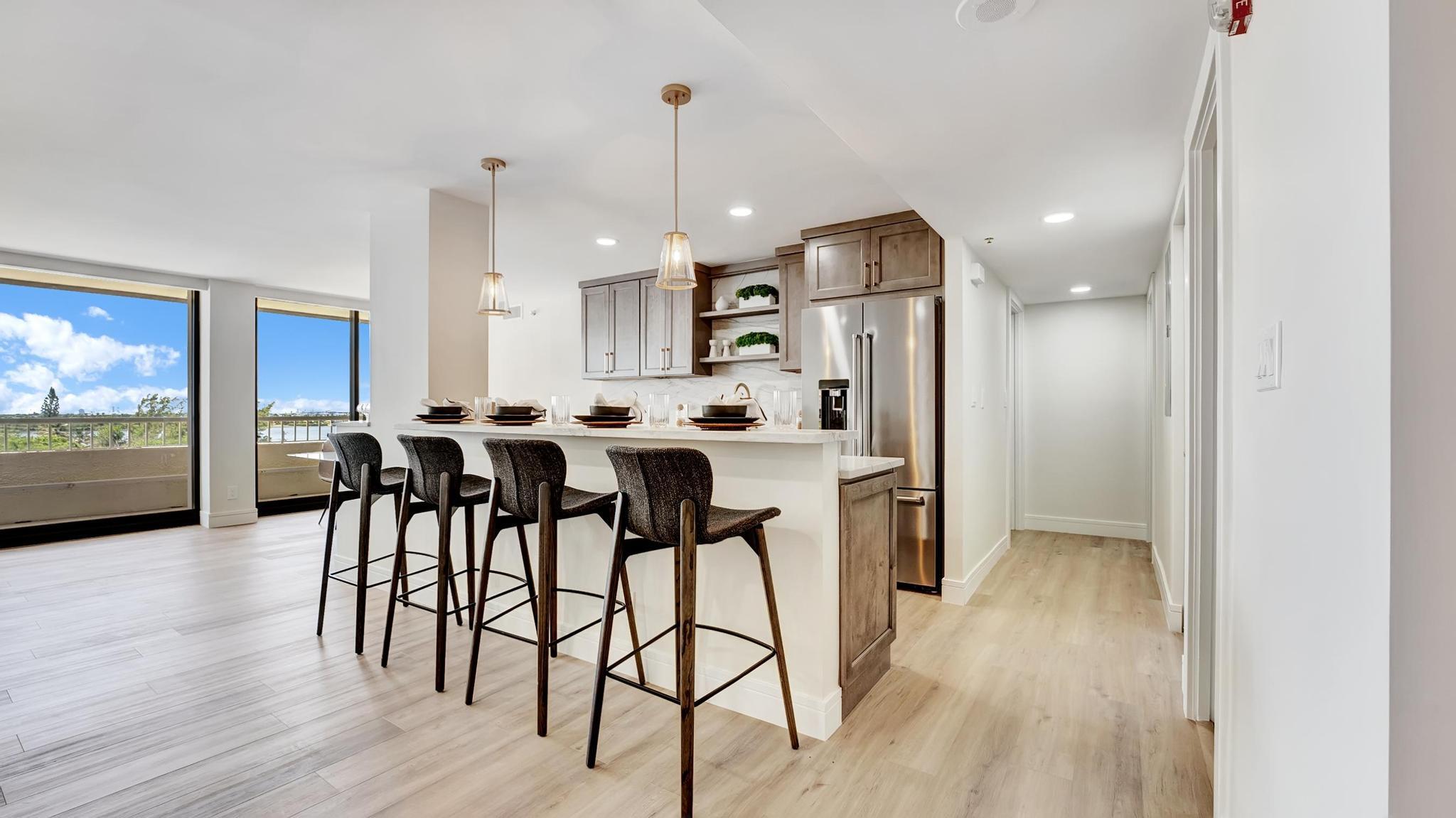 Staged condo kitchen with a four-stool breakfast bar, stainless appliances, and water views through large windows.