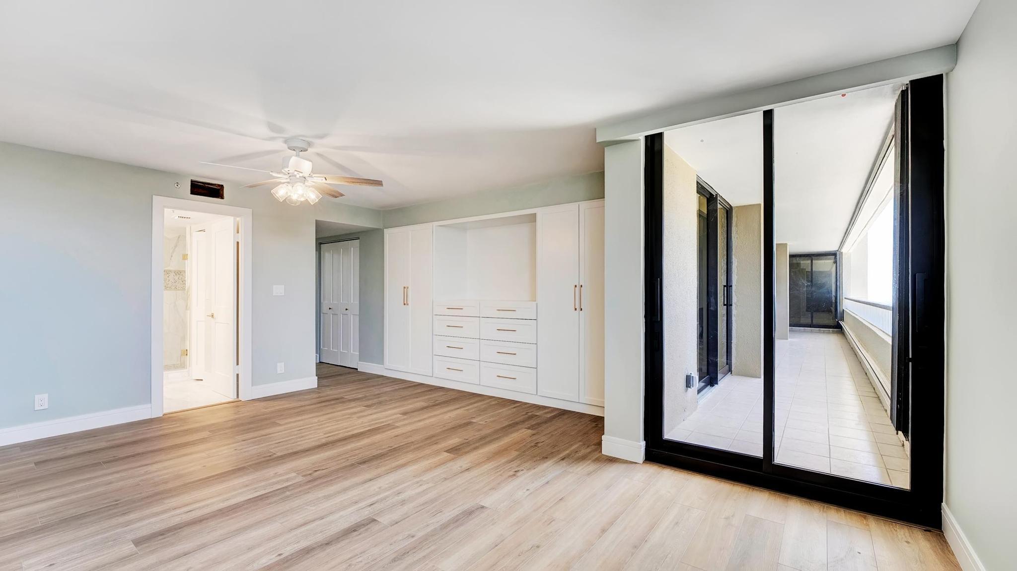 Vacant bedroom with built-in white closets and sliding glass doors to a tiled balcony.
