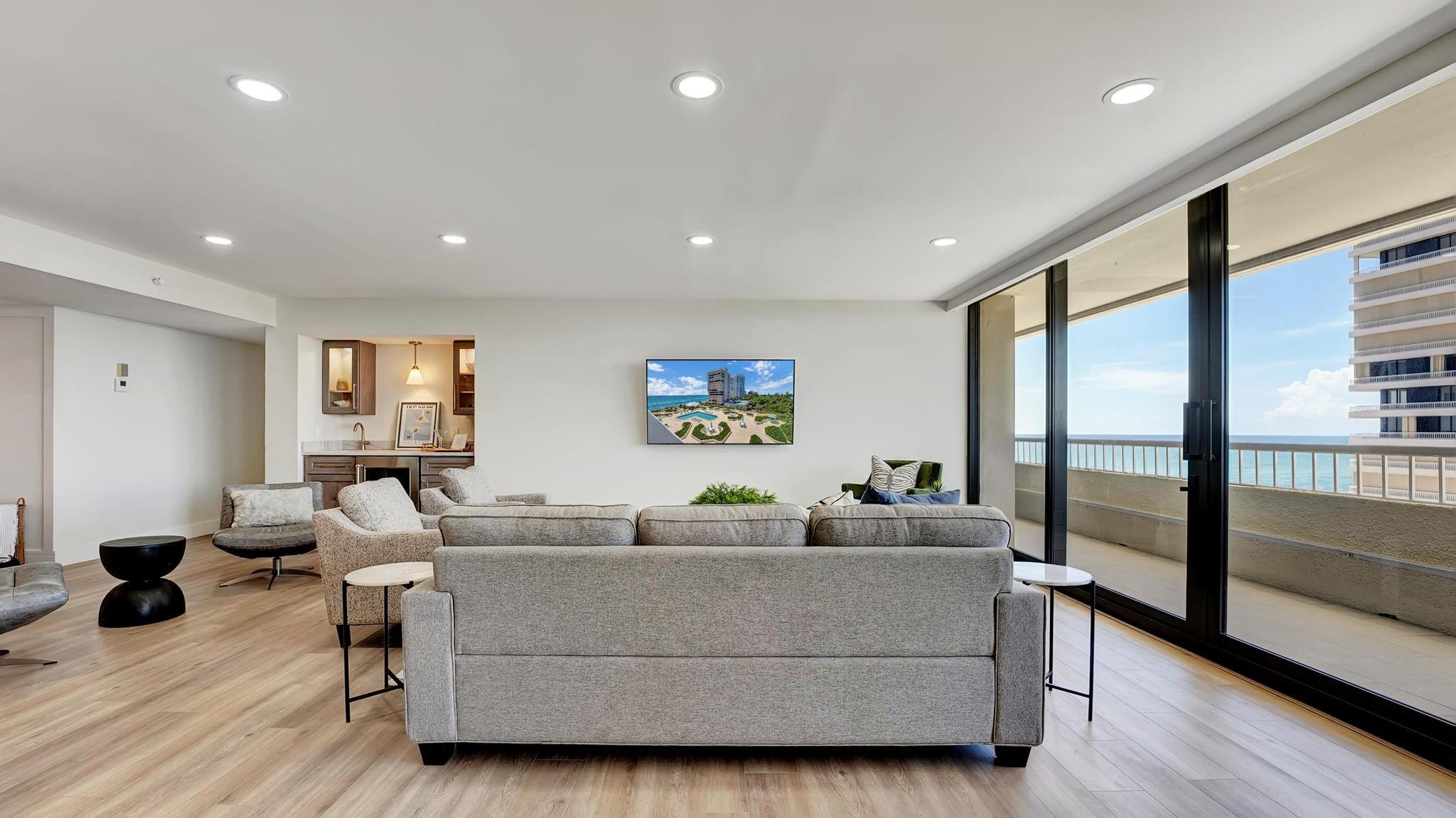 Furnished condo living room with gray sofas and sliding doors opening to an ocean-view balcony.