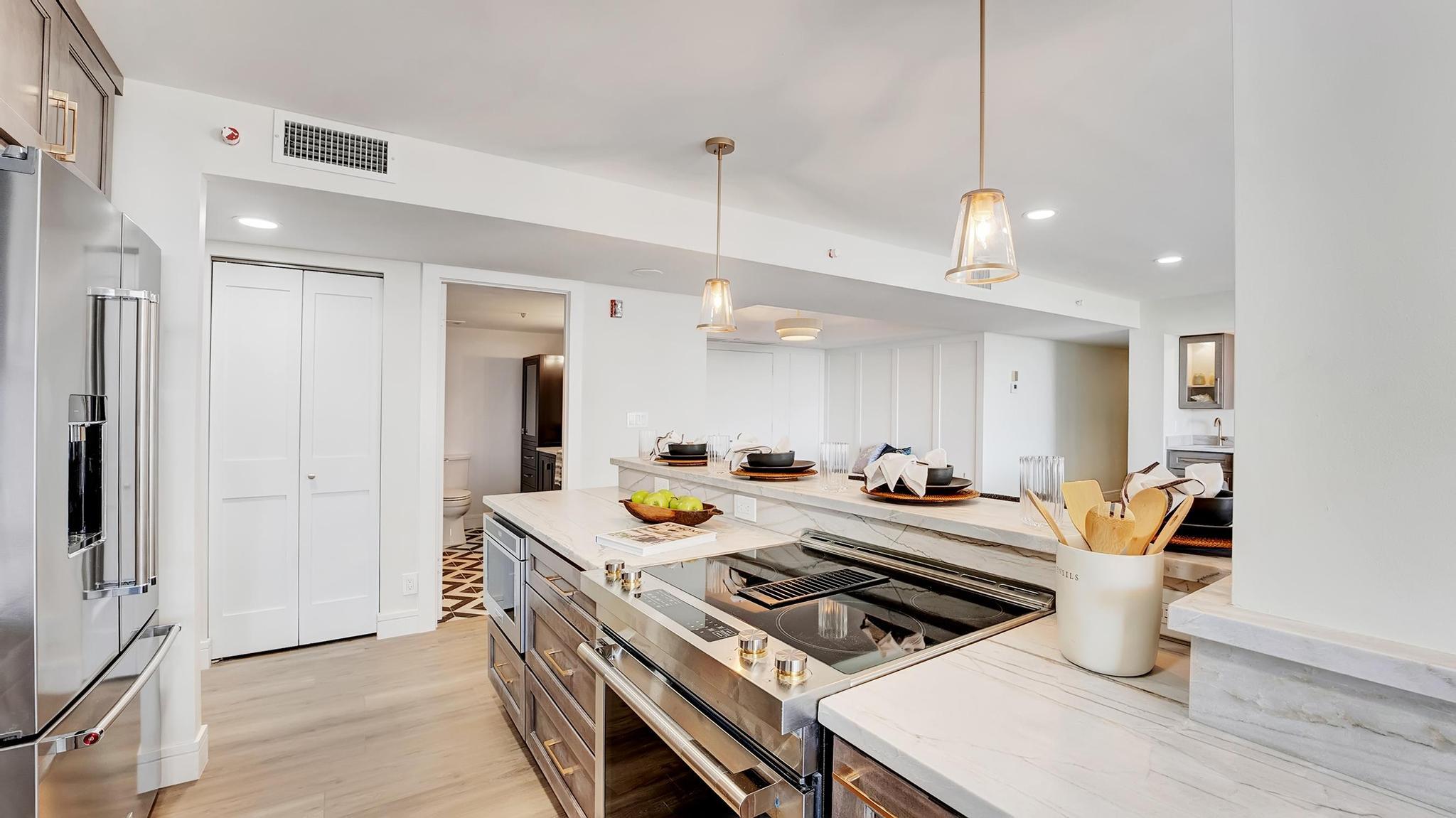 Staged modern kitchen with a marble island, built-in cooktop, stainless steel appliances, and pendant lights.